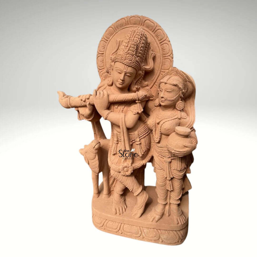 Radha Krishna Statue with Flute in Sand Stone 3ft 2 A magnificent 3-foot handcrafted Radha Krishna sandstone statue is elegantly depicted against a neutral background. This exquisite sculpture beautifully portrays Lord Krishna in his iconic posture playing the flute a timeless symbol of divine love and spiritual enchantment. He is adorned with an elaborate crown intricate jewelry and flowing garments all meticulously carved from the rich sandstone. Beside him stands Radha his beloved consort equally adorned holding a pot her gaze gently directed towards Krishna embodying their profound spiritual connection. The warm earthy tone of the sandstone accentuates the exceptional detail and artistry of the carving. Krishna's graceful posture with one leg crossed and Radha's serene stance are rendered with fluid lines conveying both movement and unwavering devotion. Behind their divine figures, a circular halo-like structure is intricately carved with traditional patterns further enhancing their divine aura. A charming small calf is positioned beside Krishna reinforcing the pastoral and idyllic setting often associated with their eternal legends. Every ornament from Krishna's anklets to Radha's elaborate earrings is clearly defined showcasing truly remarkable craftsmanship. The entire ensemble rests on a sturdy multi-layered base also handcrafted from sandstone featuring delicate lotus petal motifs and other traditional designs. This base provides a strong aesthetic foundation and elevates the statue making it a prominent display piece. This 3-foot handcrafted Radha Krishna sandstone statue embodies spiritual beauty and artistic excellence serving as a captivating subject for an article exploring such devotional and intricately crafted sculptures.