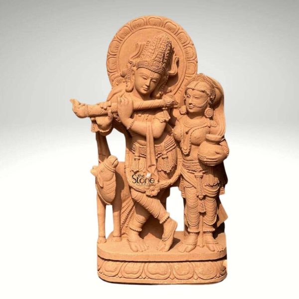 A magnificent 3-foot sandstone Radha Krishna statue with a flute is elegantly depicted against a neutral background. The sculpture beautifully portrays Lord Krishna in his iconic posture playing the flute a symbol of divine melody and enchanting love. He is adorned with an elaborate crown intricate jewelry and flowing garments all meticulously carved from the sandstone. Beside him stands Radha, his beloved consort also richly adorned holding a pot her gaze gently directed towards Krishna. The figures exude grace and a deep spiritual connection. The intricate details of the carving are highlighted by the warm earthy tone of the sandstone. Krishna's posture with one leg crossed and Radha's gentle stance, are rendered with fluid lines conveying movement and devotion. Behind their heads a circular halo-like structure is carved with traditional patterns adding to their divine aura. A small endearing calf is positioned beside Krishna reinforcing the pastoral and idyllic setting often associated with their legends. Every ornament from Krishna's anklets to Radha's earrings is clearly defined showcasing exceptional craftsmanship. The entire ensemble rests on a sturdy multi-layered base also carved from sandstone featuring delicate lotus petal motifs and other traditional designs. This base provides a strong foundation and elevates the statue making it a prominent display piece. This 3-foot Sandstone Radha Krishna statue with flute truly embodies spiritual beauty and artistic excellence making it a compelling subject for an article exploring such devotional sculptures.