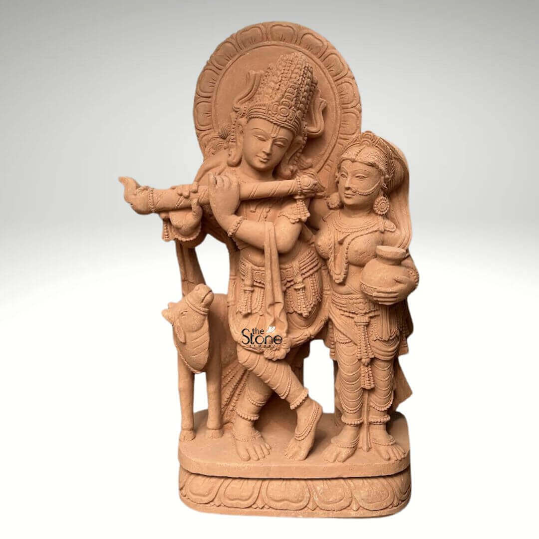 Radha Krishna Statue with Flute in Sand Stone 3ft 7 A magnificent 3-foot sandstone Radha Krishna idol is elegantly depicted against a neutral background making it a perfect centerpiece for a pooja room. The sculpture beautifully portrays Lord Krishna in his iconic posture playing the flute a symbol of divine melody, love and spiritual harmony. He is regally adorned with an elaborate crown intricate jewelry and flowing garments all meticulously carved from the rich sandstone reflecting divine artistry. Standing gracefully beside him is Radha his beloved consort equally embellished with traditional ornaments holding a pot, her gaze gently directed towards Krishna embodying their profound spiritual connection. The warm earthy hue of the sandstone magnificently enhances the intricate details and the spiritual essence of the carving. Krishna's graceful posture with one leg crossed and Radha's gentle yet dignified stance are sculpted with fluid lines conveying a sense of serene movement and unwavering devotion. Behind their divine figures a circular halo-like structure is intricately carved with traditional patterns further accentuating their divine aura and significance for a pooja room. A charming small calf is positioned intimately beside Krishna reinforcing the idyllic and pastoral setting often associated with their divine pastimes. Every ornament from Krishna's anklets and bangles to Radha's earrings and necklace is clearly defined demonstrating truly remarkable craftsmanship and attention to detail. The entire divine ensemble rests upon a sturdy, multi-layered base also meticulously carved from sandstone featuring delicate lotus petal motifs and other traditional designs. This intricately designed base provides a strong aesthetic foundation and elevates the idol making it a prominent and revered display piece. This 3-foot Sandstone Radha Krishna idol embodies both spiritual beauty and exceptional artistic excellence making it a captivating subject for an article exploring such devotional and intricately crafted statues suitable for a sacred pooja room.