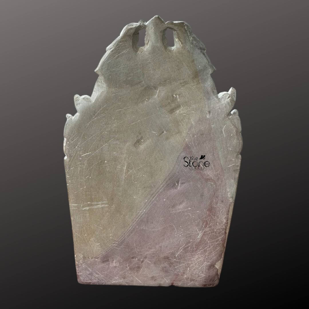 Buddha Statue 8" 6 This image shows the back of an 8-inch Lord Buddha statue carved from pink stone presented against a deep dark background. The reverse side reveals the raw unpolished texture of the stone with visible tool marks and natural variations in its surface. The overall shape is that of an elongated arch or stele tapering towards the top with a slightly irregular handcrafted outline. The natural pink hue of the stone is more apparent on this side showing subtle transitions from lighter pinks to deeper richer tones across its surface. The back of the statue does not feature intricate carvings but rather the sturdy solid mass of the stone which gives the front-facing idol its structural integrity. The edges are softly rounded indicating the craftsmanship involved in shaping the stone. The visible texture and subtle color variations add to the authenticity and natural beauty of the pink stone material. This view of the back of the 8-inch pink stone Buddha statue is important for an article about Lord Buddha statues for home decor offering insight into the material and artisanal process. While the front provides the detailed deity the back showcases the natural stone and the foundation of the sculpture emphasizing its handcrafted nature and the unique characteristics of pink stone as a medium for spiritual art in home decor.