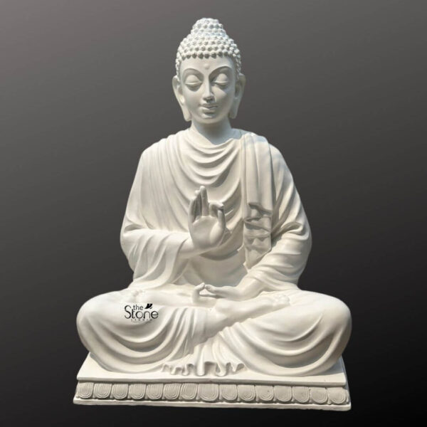 A serene full-view photograph of a 5-foot tall Buddha Fibre Idol meticulously crafted for a meditation space and presented against a simple dark gradient background that emphasizes its presence. The statue depicts Lord Buddha in a traditional peaceful seated posture known as vajrasana with both legs crossed. The idol is rendered in a smooth matte white finish which gives it the appearance of carved marble while retaining the lightweight durability of high-quality fibre. Buddha is shown with his eyes gently closed in deep contemplation a faint compassionate smile on his lips and his iconic curled hair and ushnisha clearly defined. He is draped in flowing monastic robes known as sanghati whose delicate folds are realistically sculpted adding depth and texture to the form. His right hand is raised in the vitarka mudra with the thumb and index finger forming a circle while his left hand rests in his lap palm upward in the dhyana mudra. The statue is seated upon a simple rectangular plinth that features a finely carved decorative border of stylized lotus petals providing a stable and elegant base. This large-scale Buddha Fibre Idol is an ideal centerpiece for any meditation room or spiritual corner embodying the tranquility and wisdom central to the article's theme. The craftsmanship highlights the spiritual grace of the Enlightened One making it a commanding yet peaceful focal point for reflection and mindfulness practice.