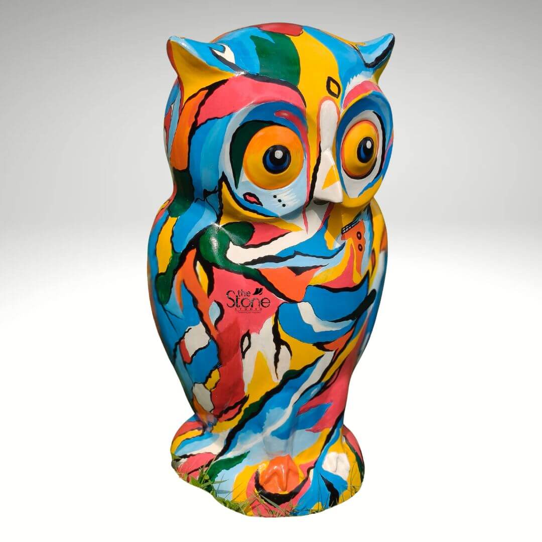 Pop Art Owl Statue 3ft 2 A vibrant three-foot-tall fibre Pop Art owl statue stands centered against a seamless light grey studio background. The sculpture is hand-painted with a dynamic and chaotic array of bold colors including bright yellow turquoise blue hot pink green orange and white applied in abstract swirling brushstrokes and geometric shapes. This kaleidoscope of color covers the entirety of the owl's form from its pointed ear tufts and large expressive eyes to its patterned chest and taloned feet. The overall aesthetic is playful energetic and characteristic of the Pop Art style making it a striking focal point. The statue is sculpted in a realistic standing owl pose but the surface treatment is entirely non-representational focusing purely on the expressive use of color and form. The large round eyes feature orange irises and dark pupils outlined in white and yellow giving them an engaging almost surprised look. The abstract pattern continues across the face creating a patchwork effect with no clear delineation of feathers save for the suggestion of a beak and ear tufts defined by the paint placement. The statue appears to be made of a durable fibre material suitable for outdoor display with a smooth painted finish. As a 36-inch Colorful Owl Garden Sculpture this piece is designed to make a significant visual impact in an outdoor setting. Its large scale and vivid colors ensure it stands out against natural greenery and landscaping embodying the fun and artistic spirit of a Pop Art garden accent. The detailed craftsmanship and bold design make it an ideal subject for an article discussing unique and artistic garden decor. The statue's sturdy construction and artistic flair make it both a decorative element and a conversation piece.