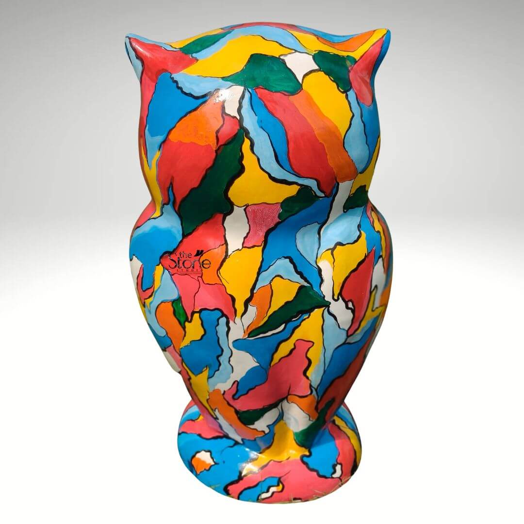 Pop Art Owl Statue 3ft 8 A vibrant three-foot-tall decorative owl sculpture stands centered against a seamless light grey studio background. The statue is a striking example of Pop Art completely covered in a dynamic chaotic pattern of large irregular color patches. The surface is a kaleidoscope of bold hues including bright yellow turquoise blue hot pink green and white all outlined with dark graphic lines that define each shape. This abstract patchwork-like design wraps entirely around the owl's form from its pointed ear tufts and head down to its base. The statue is sculpted in a realistic standing owl pose featuring prominent ear tufts and a subtle shaping of the wings and chest all of which serve as a canvas for the colorful pattern. Its face has a simplified graphic quality with the abstract shapes forming the areas around the eyes and beak giving it an engaging non-traditional look. The statue is made of a durable fibre material evidenced by its solid form and smooth painted finish suitable for both indoor and outdoor display as a piece of art. This 36-inch Fibre Pop Art Owl statue is designed to be a commanding presence as a decorative element. Its large scale and eye-catching multi-colored design make it an ideal focal point for gardens patios or large interior spaces. The Pop Art aesthetic is emphasized by the commercial almost clashing colors and the bold illustrative quality of the black outlines. This piece perfectly embodies the spirit of using everyday objects as a medium for expressive and accessible art.