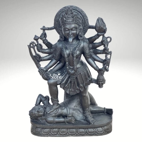 A powerful 2 feet Hand-Carved Kali Mata Sculpture meticulously crafted from dark blackstone stands dramatically against a clean light background highlighting its fierce yet protective form. This 2 feet blackstone Maa Kali statue depicts the formidable goddess Kali Mata embodying her destructive and transformative power. She is shown in her iconic stance with her right foot placed upon the reclining figure of Lord Shiva a symbolic representation of divine energy and consciousness perfectly showcasing a Hand-Carved Kali Mata Sculpture. The smooth polished blackstone gives the statue a commanding and ancient presence. Maa Kali is depicted with multiple arms each holding a different weapon or symbolic item signifying her various powers to destroy evil and ignorance. Her tongue protrudes menacingly and her face though fierce also conveys a sense of divine purpose. She wears a crown necklaces including a garland of skulls or severed heads implied by the style and a short skirt all intricately carved in the blackstone consistent with traditional iconography. A halo or aureole behind her head further emphasizes her divine status. The intricate details of her jewelry weapons including a sword trident and severed head and the expressions on her primary face showcase exceptional hand-carved craftsmanship. The reclining figure of Lord Shiva beneath her foot is also carved with clear detail serene even in this powerful pose representing the balance of cosmic forces. The entire sculpture rests on a multi-tiered lotus-petal shaped base also made of blackstone providing a sturdy and dignified foundation. The overall composition powerfully conveys Kali Mata's immense strength her role as a destroyer of evil and her ultimate protective nature. This detailed description effectively connects the visual elements of the Hand-Carved Kali Mata Sculpture with its spiritual significance and aesthetic qualities, making it an ideal representation for an article about a 2 feet blackstone Maa Kali statue.