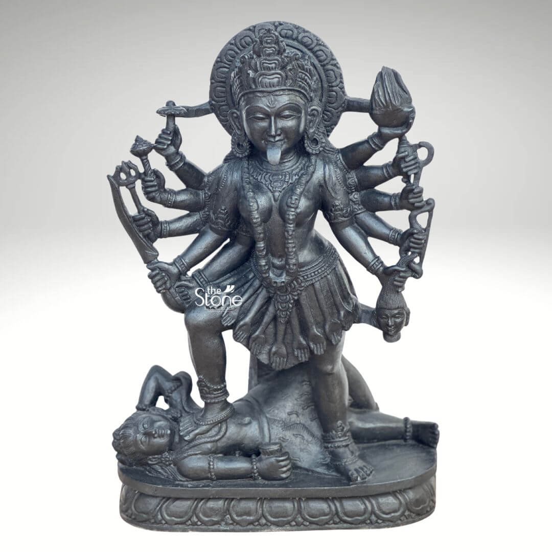 Kali Maa Murti Online 2ft 1 A powerful 2 feet Hand-Carved Kali Mata Sculpture meticulously crafted from dark blackstone stands dramatically against a clean light background highlighting its fierce yet protective form. This 2 feet blackstone Maa Kali statue depicts the formidable goddess Kali Mata embodying her destructive and transformative power. She is shown in her iconic stance with her right foot placed upon the reclining figure of Lord Shiva a symbolic representation of divine energy and consciousness perfectly showcasing a Hand-Carved Kali Mata Sculpture. The smooth polished blackstone gives the statue a commanding and ancient presence. Maa Kali is depicted with multiple arms each holding a different weapon or symbolic item signifying her various powers to destroy evil and ignorance. Her tongue protrudes menacingly and her face though fierce also conveys a sense of divine purpose. She wears a crown necklaces including a garland of skulls or severed heads implied by the style and a short skirt all intricately carved in the blackstone consistent with traditional iconography. A halo or aureole behind her head further emphasizes her divine status. The intricate details of her jewelry weapons including a sword trident and severed head and the expressions on her primary face showcase exceptional hand-carved craftsmanship. The reclining figure of Lord Shiva beneath her foot is also carved with clear detail serene even in this powerful pose representing the balance of cosmic forces. The entire sculpture rests on a multi-tiered lotus-petal shaped base also made of blackstone providing a sturdy and dignified foundation. The overall composition powerfully conveys Kali Mata's immense strength her role as a destroyer of evil and her ultimate protective nature. This detailed description effectively connects the visual elements of the Hand-Carved Kali Mata Sculpture with its spiritual significance and aesthetic qualities, making it an ideal representation for an article about a 2 feet blackstone Maa Kali statue.
