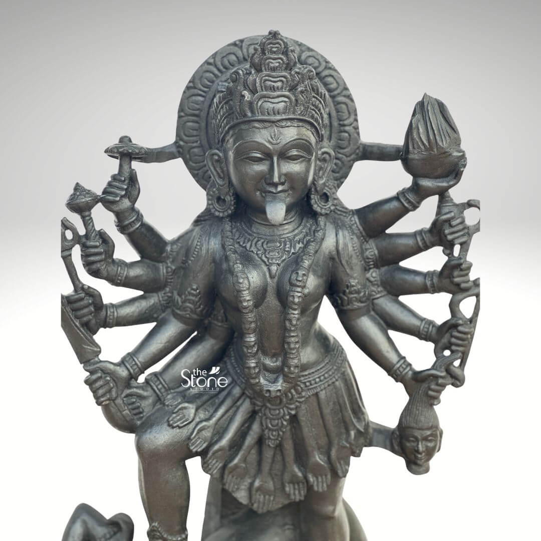 Kali Maa Murti Online 2ft 7 A close-up of a powerful 2 feet Kali Devi Black Stone Statue meticulously carved from dark blackstone is presented against a clean light background highlighting its fierce yet protective form. This 2 feet blackstone Maa Kali statue depicts the formidable goddess Kali Devi embodying her destructive and transformative power. She is shown with her tongue protruding a fierce expression and multiple arms each holding a different weapon or symbolic item signifying her various powers to destroy evil and ignorance. The smooth polished blackstone gives the statue a commanding and ancient presence. Maa Kali is adorned with a detailed crown necklaces and what appears to be a skirt of skulls or severed arms all intricately carved in the blackstone. A halo or aureole behind her head further emphasizes her divine status. The intricate details of her jewelry weapons and her dynamic posture showcase exceptional craftsmanship. The individual fingers and the distinct items held in each hand are clearly defined adding to the statue's dramatic intensity. The statue depicts her in an active dancing or striding pose with one knee slightly bent emphasizing her powerful movement. Although not fully visible, the traditional iconography usually includes her standing or dancing upon the reclining figure of Lord Shiva. The overall composition powerfully conveys Kali Devi's immense strength her role as a destroyer of evil and her ultimate protective nature. This detailed description effectively connects the visual elements of the Kali Devi Black Stone Statue with its spiritual significance and aesthetic qualities making it an ideal representation for an article about a 2 feet blackstone Maa Kali statue.