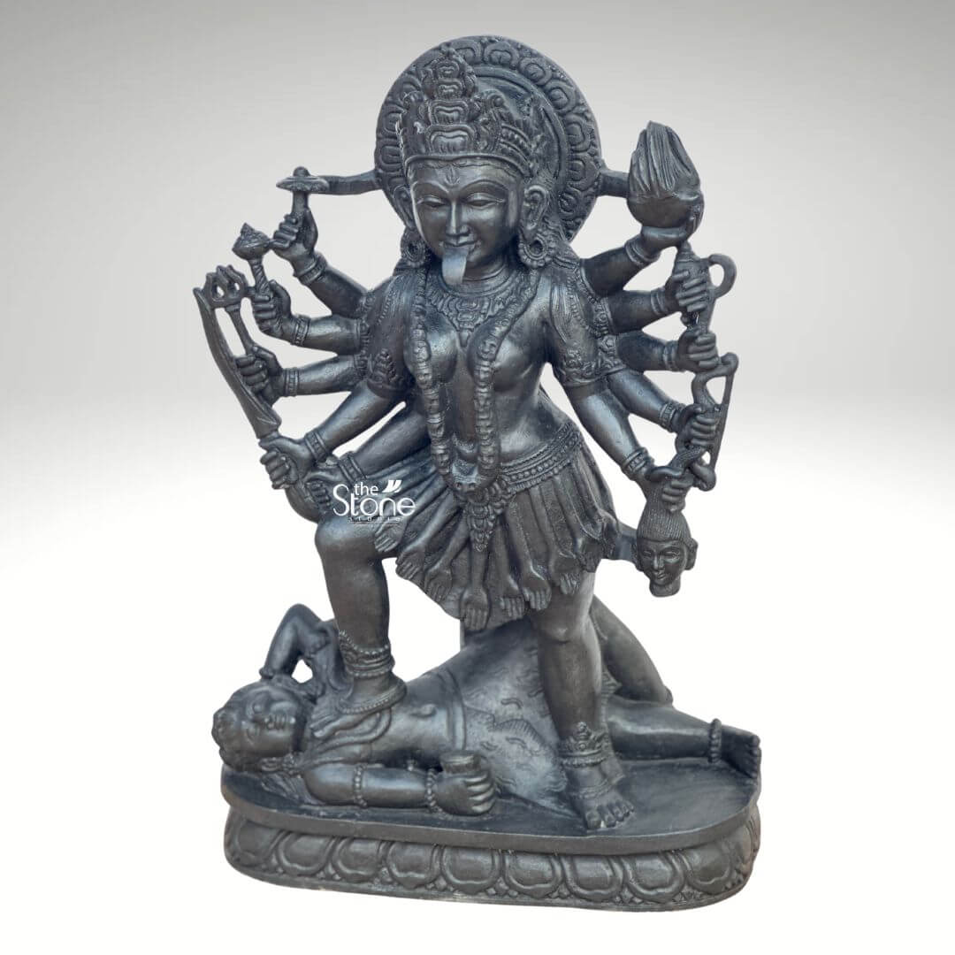 Kali Maa Murti Online 2ft 8 A powerful 2 feet Kali Mata Black Stone Murti meticulously carved from dark blackstone stands dramatically against a clean light background highlighting its fierce yet protective form. This 2 feet blackstone Maa Kali statue depicts the formidable goddess Kali Mata embodying her destructive and transformative power. She is shown in her iconic stance with her right foot placed upon the reclining figure of Lord Shiva a symbolic representation of divine energy and consciousness perfectly capturing the essence of a Kali Mata Black Stone Murti. The smooth polished blackstone gives the statue a commanding and ancient presence. Maa Kali is depicted with multiple arms each holding a different weapon or symbolic item signifying her various powers to destroy evil and ignorance. Her tongue protrudes menacingly and her face though fierce, also conveys a sense of divine purpose. She wears a crown necklaces (including a garland of skulls or severed heads implied by the style and a skirt, all intricately carved in the blackstone consistent with traditional iconography. A halo or aureole behind her head further emphasizes her divine status. The intricate details of her jewelry weapons and the expressions on her primary face showcase exceptional craftsmanship. The reclining figure of Lord Shiva beneath her foot is also carved with clear detail serene even in this powerful pose representing the balance of cosmic forces. The entire sculpture rests on a multi-tiered lotus-petal shaped base also made of blackstone providing a sturdy and dignified foundation. The overall composition powerfully conveys Kali Mata's immense strength her role as a destroyer of evil and her ultimate protective nature. This detailed description effectively connects the visual elements of the Kali Mata Black Stone Murti with its spiritual significance and aesthetic qualities, making it an ideal representation for an article about a 2 feet blackstone Maa Kali statue.