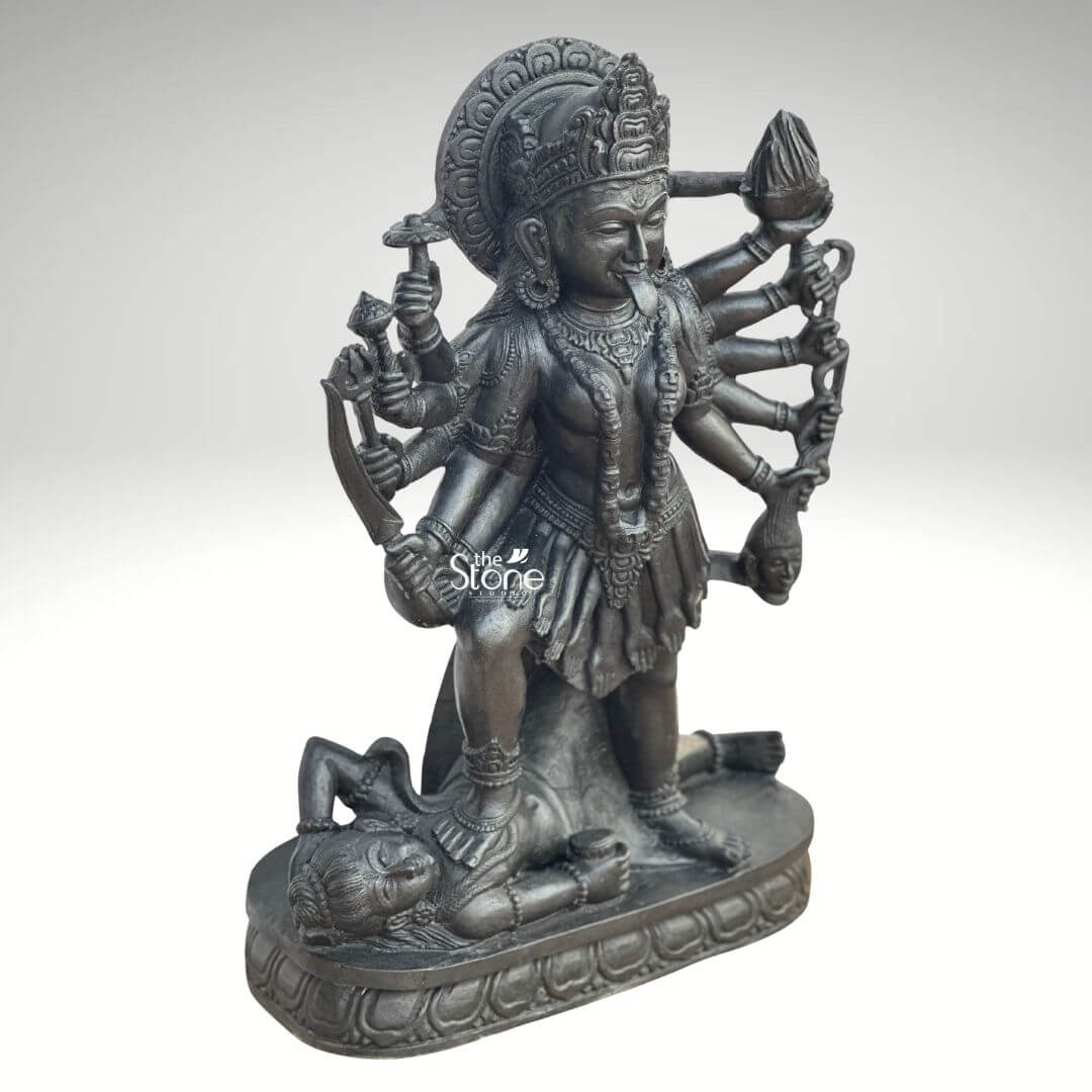 Kali Maa Murti Online 2ft 10 A powerful 2 feet Traditional Mahakali Stone Idol meticulously carved from dark blackstone stands dramatically against a clean light background highlighting its fierce yet protective form. This 2 feet blackstone Maa Kali statue depicts the formidable goddess Mahakali embodying her destructive and transformative power. She is shown in her iconic stance with her right foot placed upon the reclining figure of Lord Shiva a symbolic representation of divine energy and consciousness perfectly capturing the essence of a Traditional Mahakali Stone Idol. The smooth polished blackstone gives the statue a commanding and ancient presence consistent with traditional sculptural forms. Maa Kali is depicted with multiple arms each holding a different weapon or symbolic item signifying her various powers to destroy evil and ignorance. Her tongue protrudes menacingly and her face though fierce also conveys a sense of divine purpose. She wears a crown necklaces implied and a short skirt all intricately carved in the blackstone adhering to traditional iconography. A halo or aureole behind her head further emphasizes her divine status. The intricate details of her jewelry weapons and the expressions on her primary face showcase exceptional craftsmanship. The reclining figure of Lord Shiva beneath her foot is also carved with clear detail serene even in this powerful pose representing the balance of cosmic forces. The entire sculpture rests on a multi-tiered lotus-petal shaped base also made of blackstone, providing a sturdy and dignified foundation, typical of traditional idols. The overall composition powerfully conveys Mahakali's immense strength, her role as a destroyer of evil, and her ultimate protective nature. This detailed description effectively connects the visual elements of the "Traditional Mahakali Stone Idol" with its spiritual significance and aesthetic qualities, making it an ideal representation for an article about a 2 feet blackstone Maa Kali statue.