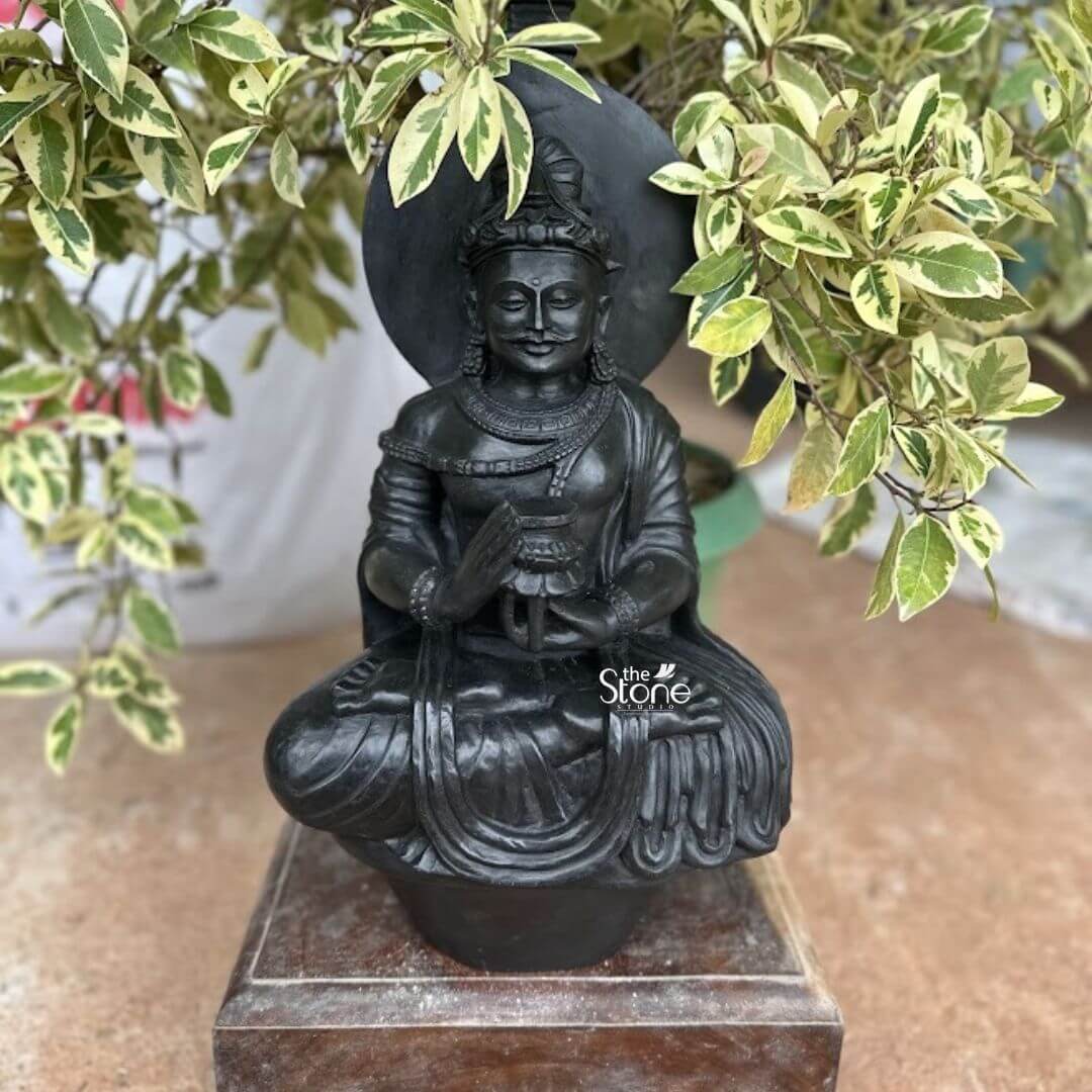 Bodhisattva Meditating Sculpture 2ft 3 A captivating 2-foot Blackstone Bodhisattva statue presented as a Unique Buddha Antique Sculpture for Table Top is gracefully displayed on a wooden base set against a vibrant backdrop of variegated green and white foliage. The statue carved from deep lustrous black stone depicts a Bodhisattva figure seated in a meditative posture likely the full lotus position. Unlike typical Buddha statues this figure features a distinct mustache and a more ornate regal appearance hinting at a specific Bodhisattva or an earlier less ascetic portrayal of enlightenment making it truly unique and antique in style. The figure is richly adorned with an elaborate crown multiple layers of intricate jewelry including necklaces armlets and possibly a sacred thread. His hands are held in a gesture of holding an alms bowl or a sacred vessel symbolizing generosity and the accumulation of merit. The black stone's smooth finish highlights these fine details creating a striking contrast with the lighter elements and bringing out the exquisite craftsmanship. A circular halo or aureole frames his head further emphasizing his divine and enlightened presence. The statue rests on a simple yet sturdy dark wooden base which is itself placed on a warm reddish-brown surface possibly a terracotta patio or shelf. The surrounding potted plant with striking green and white leaves creates a lush natural backdrop enhancing the statue's serene and contemplative presence. This 2-foot Blackstone Bodhisattva statue is an exquisite example of religious artistry with an antique feel designed to bring blessings peace and a unique aesthetic beauty to any home making it an ideal focal point for a table top perfectly aligning with an article focusing on distinctive and antique Buddha sculptures for decor.