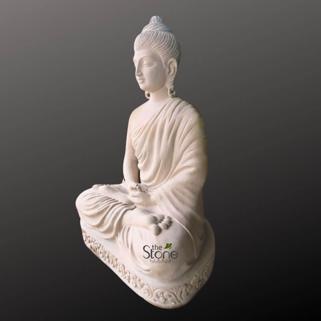 Zen Garden Buddha Statue 3.5ft 14 beautifully carved, light-colored stone statue of Buddha is depicted in a meditative pose, likely crafted from white marble, sandstone, or alabaster, showcasing meticulous detail and smooth finish. The Buddha is seated in the traditional Padmasana (full lotus) position, with legs crossed and feet resting on the opposite thighs. His hands are gently placed in his lap in the Dhyana Mudra, signifying meditation and inner peace, with palms upward and the right hand resting on top of the left, thumbs lightly touching. The Buddha's face conveys profound serenity and contemplation, with gracefully closed or downcast eyes, a soft, subtle smile, and elongated earlobes, traditional symbols of wisdom and compassion. An 'urna,' a prominent dot or jewel, is visible between his eyebrows, representing a spiritual third eye. His hair is intricately sculpted into tight, coiling curls that form a distinct 'ushnisha,' the cranial protuberance at the crown, symbolizing spiritual wisdom and enlightenment. The flowing monastic robes are artfully draped over his left shoulder and across his body, with naturalistic, deep folds that highlight the contours of the figure and convey a sense of lightness and movement despite the rigid stone medium. The statue rests upon an ornate, richly detailed base, featuring deeply carved, symmetrical floral or vine-like patterns that add to the piece's artistic elegance and craftsmanship. The entire statue is presented against a clean, gradient dark gray to black background, which expertly isolates the figure and accentuates its light color and intricate textures. Soft, directional lighting illuminates the statue, emphasizing its smooth curves and delicate carvings, giving it an almost luminous quality. A subtle watermark or logo, "the Stone Studio," is visible in the lower right, suggesting this piece is an example of high-quality, handcrafted stone sculpture, likely presented as a product or a showcase of the studio's expertise in creating spiritual art, garden statues, or decorative pieces for tranquil indoor and outdoor spaces, fostering a sense of calm and spiritual reflection.