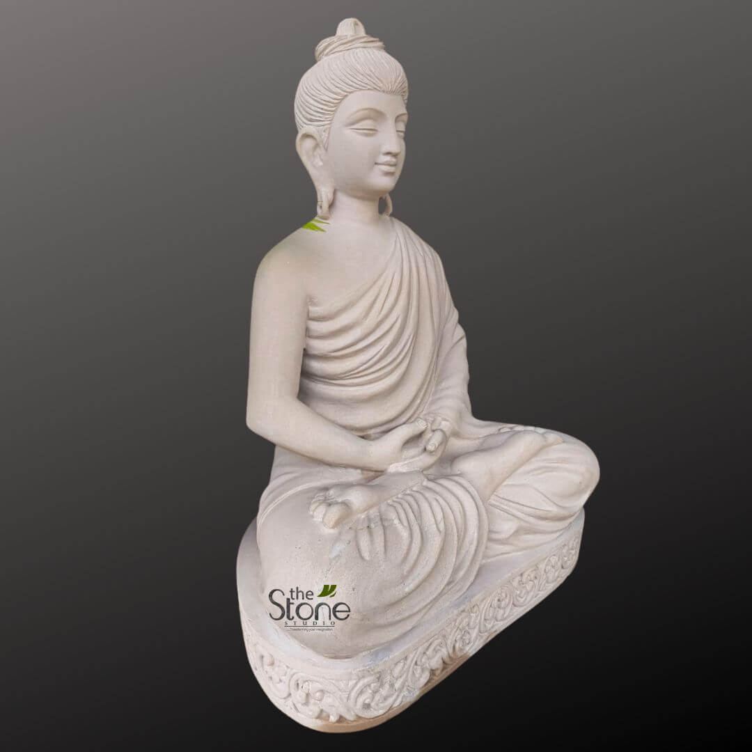 Zen Garden Buddha Statue 3.5ft 9 serene, off-white or light beige stone Buddha statue, meticulously carved and presented against a plain dark gray, subtly gradient background that helps the light-toned sculpture stand out. The Buddha is depicted in a full lotus position (Padmasana), seated upright with legs crossed, radiating an aura of deep tranquility and contemplation. His hands rest gently in his lap, palms upward, with thumbs almost touching, forming the Dhyana Mudra, a classic gesture symbolizing profound meditation and concentration. The facial features are exquisitely detailed, showing a calm, meditative expression with eyes gently closed or downcast, conveying inner peace. Traditional iconographic elements include elongated earlobes and the Ushnisha topknot on his head, signifying wisdom. His flowing robe, or Sanghati, drapes gracefully over his left shoulder and body, with naturalistic, deep folds that convey movement and softness, leaving his right shoulder and arm subtly bare. A subtle green mark, possibly a leaf or a small natural pigment, is visible on his left shoulder, adding a touch of organic detail. The statue rests upon an elegantly carved, matching stone base, which is adorned with intricate, traditional relief patterns around its edge, adding to its artistic and spiritual appeal. The "the Stone Studio" logo, featuring the brand name and a small leaf icon, is clearly visible on the lower left side of the base, indicating the craftsmanship and origin of this beautiful spiritual sculpture. This piece exemplifies traditional Buddhist art and stone carving, ideal for creating a peaceful ambiance in a home, garden, or meditation space, and serves as a visual embodiment of mindfulness, serenity, and high-quality artisan craftsmanship.