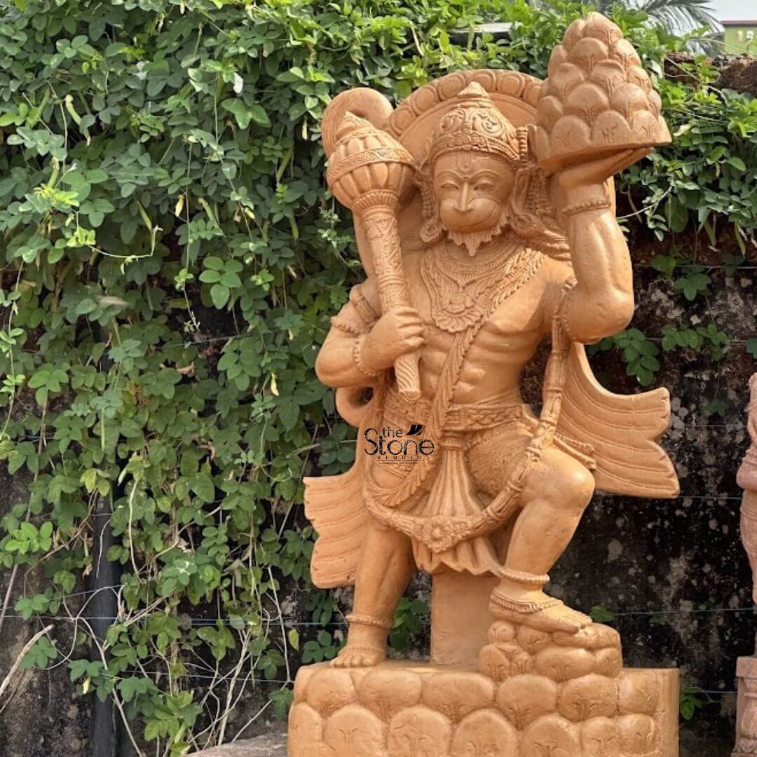 Anjaneya swamy statue 4ft 3 A magnificent 4-foot Brown Sandstone Hanuman statue dramatically depicting Bajrangbali Holding Mountain stands powerfully in an outdoor setting against a lush green vine-covered wall. The statue carved from warm reddish-brown sandstone captures Lord Hanuman in a dynamic action-filled posture with one knee bent and the other leg extended conveying immense strength and determination. He is richly adorned with an elaborate crown traditional jewelry and flowing garments all intricately sculpted to highlight his heroic form. The central and most iconic aspect directly related to the article's title is Hanuman's feat of carrying the Sanjeevani mountain. In his upper left hand he powerfully holds aloft a intricately carved miniature mountain signifying his epic journey to retrieve the life-saving herb. In his upper right hand he grasps his formidable gada emphasizing his valor and might. His facial features including his expressive eyes and determined mouth convey fierce devotion and unparalleled strength capturing the essence of Bajrangbali. The musculature of his body is clearly defined showcasing his legendary physical prowess. The statue rests on a robust multi-tiered pedestal carved with cloud or rock-like formations symbolizing the height from which he carries the mountain. The natural green backdrop of dense vines and foliage creates a vibrant contrast with the warm sandstone making the statue stand out as a powerful focal point. This 4-foot Brown Sandstone Hanuman statue is an exquisite example of religious artistry ideal for a garden or outdoor space designed to inspire awe and devotion perfectly aligning with an article focusing on Bajrangbali's legendary act of carrying the mountain.