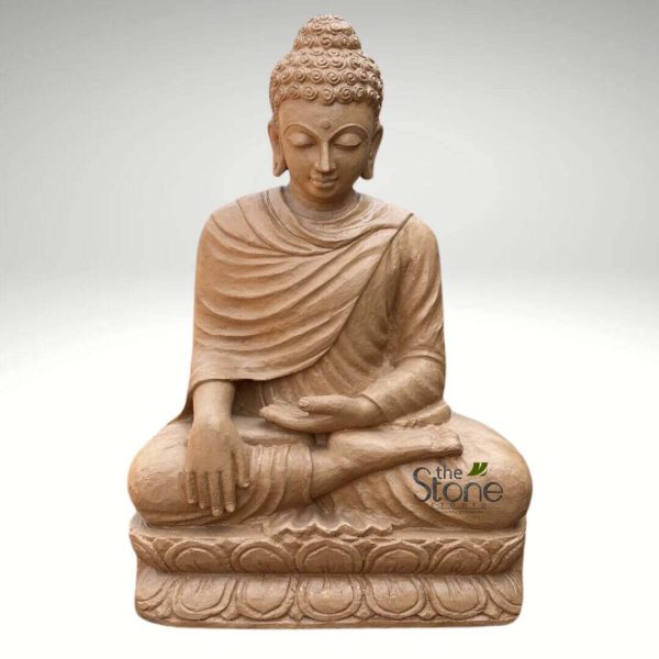 serene, full-body statue of Buddha, crafted from light brown or sand-colored natural stone, likely sandstone, stands centered against a clean, plain light grey background. The sculpture depicts Siddhartha Gautama in a traditional meditative cross-legged posture, known as Padmasana or the lotus position, symbolizing deep stability and enlightenment. His hands are gently placed in his lap, palms open and facing upwards, with the right hand resting over the left, forming the Dhyana Mudra, which represents profound contemplation, wisdom, and inner peace. The Buddha's face exudes a profound sense of tranquility and serenity, with eyes softly closed or downcast in a state of deep meditation. A subtle, peaceful smile plays upon his lips, and the traditional urna mark, a dot symbolizing spiritual insight, is visible between his eyebrows. His head features tightly coiled hair forming a distinctive ushnisha (topknot), an iconographic symbol of his awakened consciousness and spiritual wisdom. The flowing drapery of his monastic robes is intricately carved, showing realistic folds and creases that add texture and depth to the stone sculpture. The entire figure is seated upon a beautifully detailed double-lotus pedestal, with each petal distinctly carved, further enhancing its spiritual and aesthetic appeal. The earthy tones of the stone create a natural and grounding feel. A subtle brand logo, "the Stone Studio," is visible on the lower right portion of the lotus base, indicating the artisan or vendor. This exquisite Buddha sculpture is ideal for articles on spiritual wellness, meditation practices, Buddhist philosophy, serene home decor, garden statues, or the artistry of stone carving, evoking feelings of calm, mindfulness, and sacred tranquility.
