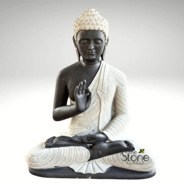 beautifully sculpted, two-tone stone statue of Buddha is depicted seated in the traditional full lotus position (Padmasana), a posture symbolizing deep meditation, spiritual awakening, and inner peace. The statue is primarily crafted from two contrasting materials or finishes: the body, face, and base are a dark, charcoal-grey or black stone, while the intricately draped robe, the distinct ushnisha (cranial bump symbolizing wisdom), and the tight curls of hair are rendered in a lighter, off-white or cream-colored stone. Buddha's face conveys profound serenity and calm, with eyes gently closed or cast downwards in meditation, a subtle, peaceful smile, and elongated earlobes, characteristic of Buddhist iconography. His right hand is raised in a gesture known as the Vitarka Mudra, where the thumb and index finger touch to form a circle, while the other fingers extend upwards. This mudra symbolizes teaching, discussion, and the transmission of wisdom or the Dharma. The robe features finely carved, flowing pleats and folds, gracefully draped over his left shoulder and across his lap, highlighting the artisanal craftsmanship of the piece. The contrasting textures between the darker, perhaps rougher stone of the body and the smoother, lighter stone of the robe add significant depth and visual interest. The statue is presented against a clean, minimalist light grey background, which emphasizes its form and details without distraction. A subtle watermark for "The Stone Studio" is visible on the lower right side of the statue, indicating its origin or artisan producer. This elegant and contemplative sculpture serves as a powerful symbol of mindfulness, spiritual balance, and tranquility, making it ideal for meditation spaces, home decor focused on Zen aesthetics, or as a unique piece showcasing traditional stone carving artistry and spiritual symbolism.