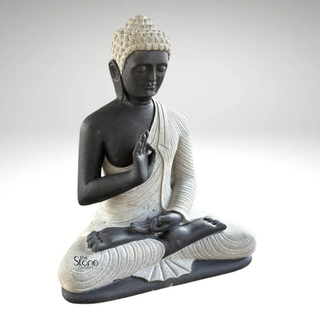 2.5ft Buddha Sculpture for Garden 4 A captivating 2.5-foot Buddha idol crafted from black stone with elegant white accents depicted in a classic meditative posture as featured in an article about Buddha idols of this size. The statue presents the Buddha seated cross-legged with his right hand raised in the Vitarka Mudra and his left hand resting in his lap in the Dhyana Mudra. The body is sculpted from a dark almost black stone providing a striking contrast to the lighter off-white or grey stone used for his robes and the tightly curled hair on his head. The robes are meticulously carved with flowing realistic folds and pleats suggesting the soft drape of fabric adding a sense of serenity and detail to the sculpture. The Buddha's face is characterized by a calm and contemplative expression,with downcast yes a gentle nose and subtle lips embodying profound inner peace and enlightenment. The tightly curled hai a distinctive iconographic feature is intricately textured in the lighter stone adding depth and authenticity. His elongated earlobes another symbolic feature are also clearly visible. The overall design of this 2.5-foot black stone Buddha statue showcases a harmonious blend of two contrasting stone colors enhancing its visual appeal and artistic merit. The smooth contours and fine details throughout the sculpture emphasize a deep sense of tranquility and spiritual harmony making it an ideal piece for personal contemplation meditation spaces or as a distinguished decorative element as discussed in the accompanying article.