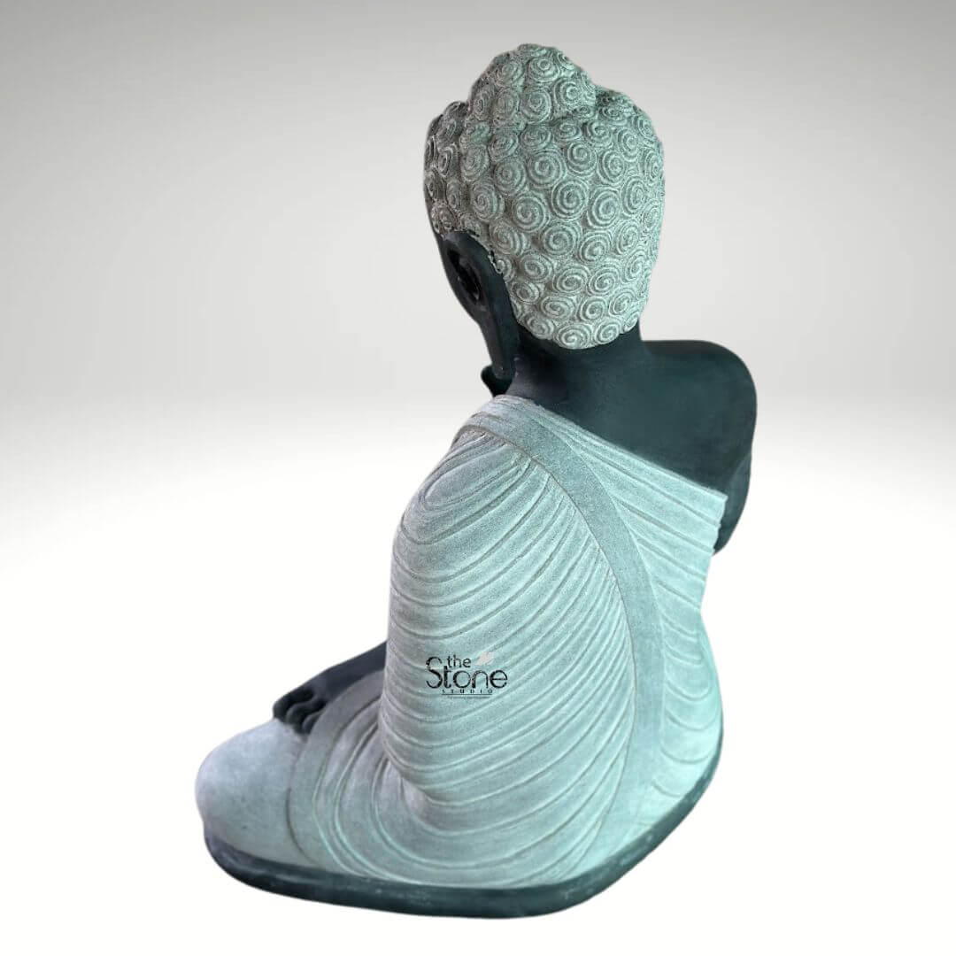 2.5ft Buddha Sculpture for Garden 9 A serene 2.5-foot granite Buddha statue in dual color crafted from black stone with contrasting lighter stone for the robes and hair viewed from a rear-right angle as detailed in an article about such sculptures. The Buddha is depicted in a seated meditative posture with his right hand gently raised in a mudra and his left hand resting in his lap. The main body of the statue including his back right arm and exposed skin is sculpted from a deep almost black stone providing a strong, grounding presence. The robes which gracefully drape over his left shoulder and cover his lower body are rendered in a contrasting lighter off-white or light grey stone. The meticulous carving of the robes showcases realistic flowing folds and pleats suggesting the soft drape of fabric and adding a sense of serenity and refined detail. The tightly curled hair on his head a distinctive iconographic feature is intricately textured in the lighter stone with individual curls clearly defined adding depth and authenticity to the sculpture. His elongated earlobes are also visible. The dual-color effect of the black and lighter granite creates a striking visual contrast that enhances the artistic appeal and spiritual essence of the piece. The smooth contours and fine details throughout the sculpture emphasize a deep sense of tranquility and spiritual harmony. This 2.5-foot granite Buddha statue is an ideal piece for personal contemplation meditation spaces or as a distinguished decorative element embodying the peaceful and enlightened nature of the Buddha as discussed in the accompanying article on dual-color granite Buddha statues.