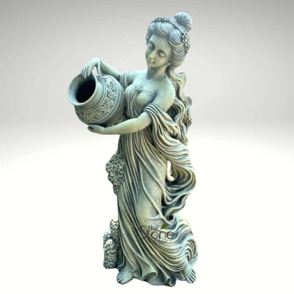 magnificent, full-length classical garden statue depicting a graceful female figure, crafted from weathered stone or a similar durable material like concrete or cast cement. The statue stands tall, viewed from a slightly elevated angle against a plain, soft grey background that emphasizes its form and intricate details. The woman is elegantly dressed in flowing, neoclassical-style drapery that cascades around her body, creating soft folds and movement, especially around her legs and arms. Her posture is serene and poised, with her head gently tilted downwards and her eyes subtly closed or cast low, conveying a sense of calm contemplation or gentle effort, as if in the act of pouring. She holds a decorative, ornate amphora-like urn or jug with both hands, tipping it forward as if pouring water from its wide mouth. The urn itself is adorned with intricate relief carvings of floral or scroll patterns. Her hair is styled in an elaborate bun atop her head, secured with what appears to be a wreath or headband of small flowers, with long, wavy tresses falling gracefully over her shoulders and down her back. Intricate carvings of grapevines and clusters of grapes are visible along the lower portion of her gown and at the base of the statue, hinting at themes of abundance, nature, or possibly Dionysian symbolism. The entire piece exhibits a beautiful aged patina, a rich, muted green-grey color that suggests years of exposure to the elements, characteristic of antique garden ornaments or weathered outdoor sculptures. This exquisite stone art piece evokes timeless beauty and would be a striking focal point for landscaping projects, patio decor, or traditional garden designs, suitable as a water feature or a standalone decorative sculpture, emphasizing its craftsmanship and enduring appeal as a quality outdoor product.