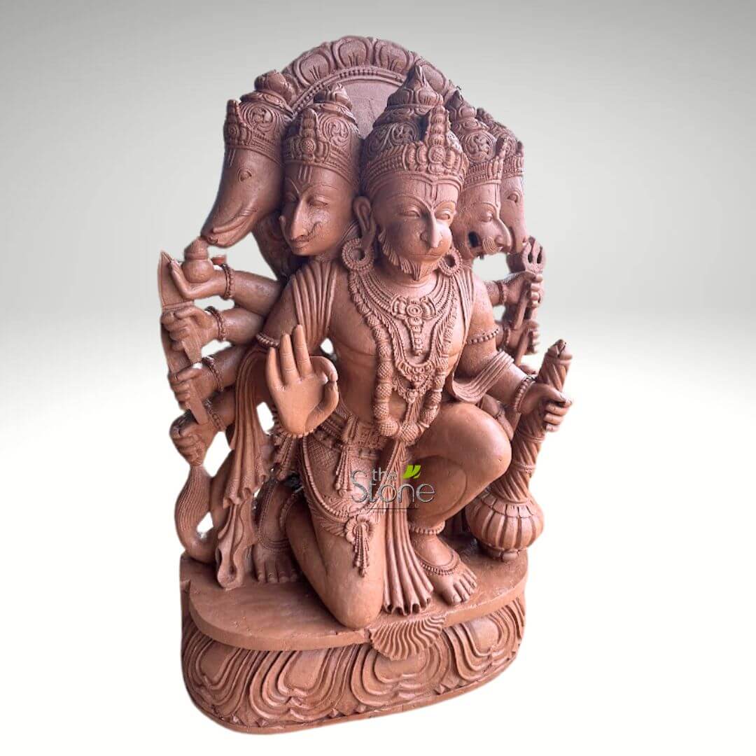 4 Feet Panchamukhi Hanuman Statue 6 detailed, reddish-brown stone or terracotta sculpture depicts Panchamukhi Hanuman, the five-faced manifestation of the Hindu deity Hanuman, captured in a powerful and dynamic kneeling or crouching pose on his right leg. The central, dominant face is that of Hanuman, a monkey-god, rendered with a distinctive snout, prominent eyes, a small beard-like texture on his chin, and an elaborate crown. Radiating from behind and around Hanuman's central head are four additional divine faces, symbolizing various protective aspects and forms. To the viewer's far left, an elephant head, representing Ganesha, is visible. Adjacent to Hanuman's left, a human-like face, potentially Garuda or another deity, can be seen. To Hanuman's right, a fierce lion head, symbolizing Narasimha, is prominently featured. Lastly, to the far right, a boar head, representing Varaha, completes the five heads. Each head wears a distinct, ornate crown. The deity is multi-armed, with eight arms in total, gracefully extending from his torso. Hanuman's prominent front right hand is raised in the abhaya mudra, a gesture of fearlessness, protection, and reassurance. His front left hand rests near his knee, firmly grasping a gada (mace), a symbol of strength and authority. Other hands hold various divine attributes and weapons; for instance, a bow and arrow are held by an arm associated with the Ganesha head, and a trident or a similar staff is visible in another rear arm. Intricate carvings adorn the sculpture, detailing elaborate necklaces, armbands, waistbands, and draped clothing across the deity's body, highlighting the traditional Indian sculptural craftsmanship. The entire sculpture rests upon a robust, multi-layered pedestal, adorned with stylized lotus petal motifs that add to its aesthetic and spiritual significance. The reddish-brown material, possibly terracotta or finely carved sandstone, has a matte finish, emphasizing the depth and texture of the intricate details. The statue is professionally lit against a plain, light grey to white gradient background, which serves to isolate and highlight its form. This powerful representation of Panchamukhi Hanuman symbolizes unified divine strength, protection from evil, and the multifaceted nature of spiritual power in Hindu mythology and is often revered for devotion, removing obstacles, and bestowing courage.