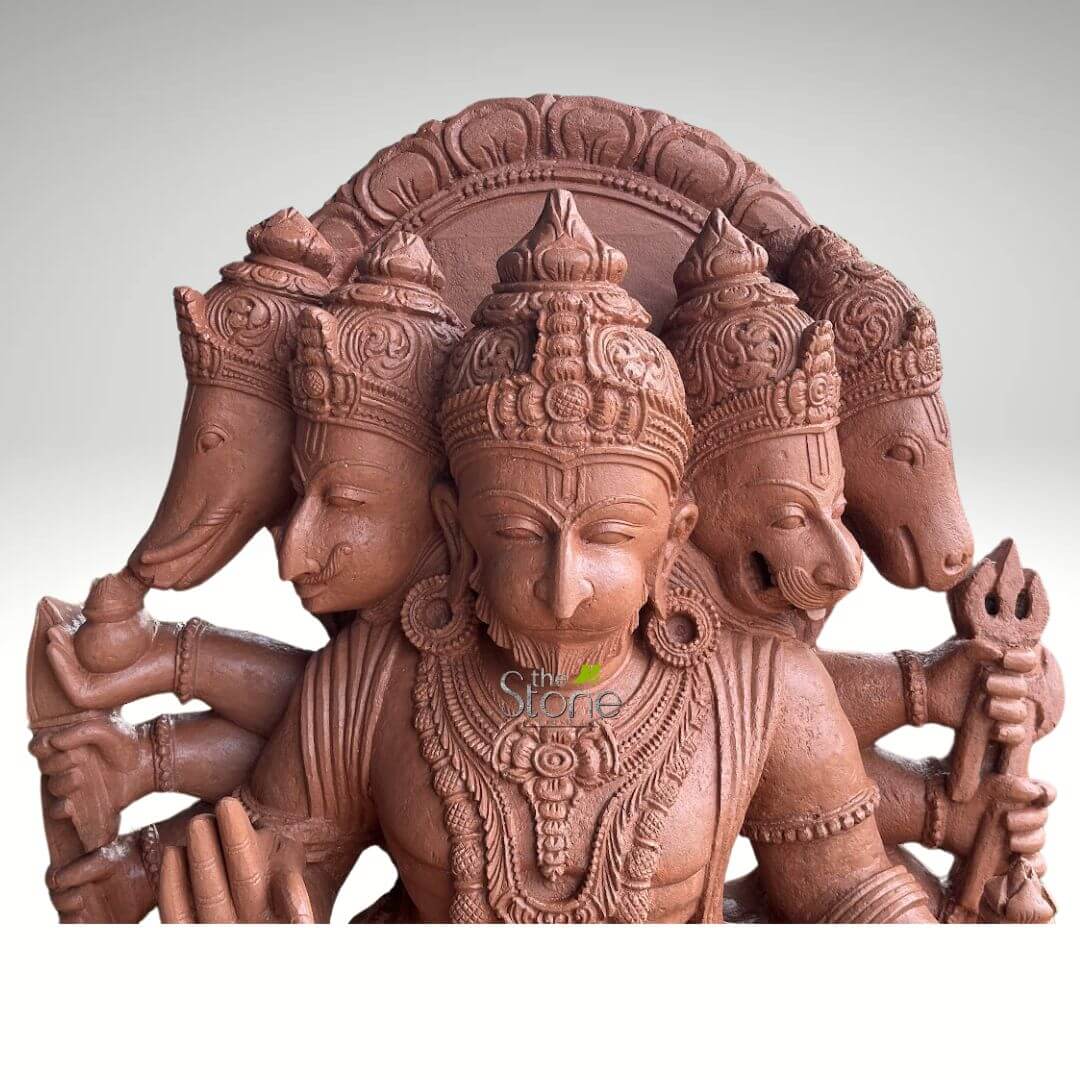 4 Feet Panchamukhi Hanuman Statue 4 meticulously crafted reddish-brown terracotta or sandstone sculpture depicting a powerful, multi-faceted Hindu deity, commonly known as Panchamukhi (five-faced). The central, dominant figure is a serene, human-like visage with closed eyes, adorned with an elaborate tiered crown, large circular earrings, and intricate necklaces, all deeply carved into the material. To the immediate left of the central face is another human-like face, distinguished by a finely sculpted mustache and a smaller crown. Further to the left, the outermost head is that of Ganesha, clearly identifiable by its elephant trunk, which appears to hold a small, round object or offering. The visible left arm of the deity, originating from this side, holds what resembles a Kamandalu (water pot) or a small vessel. To the immediate right of the central face is a fierce, leonine (lion-like) head, possibly representing Narasimha or a ferocious aspect of Shiva, characterized by an open mouth revealing sharp teeth and a powerful expression. The outermost head on the right is that of a bull, likely Nandi, Lord Shiva's sacred mount and attendant. The visible right arm of the deity holds a meticulously detailed Trishul (trident), a prominent symbol of Lord Shiva, with the prongs clearly visible. The entire sculpture showcases exceptional traditional craftsmanship, with every crown, piece of jewelry, and facial feature exhibiting fine, deeply carved details, creating a rich texture and depth. The material appears to have a slightly granular, earthy quality, suggestive of terracotta or a finely ground stone, emphasizing its artisanal nature. The deity's torso is also visible, adorned with a beaded necklace and a prominent medallion at the chest. The sculpture is presented against a plain, light gray background, allowing its intricate details and rich reddish-brown hue to stand out prominently. This sculpture serves as a potent visual representation of cosmic unity, the diverse manifestations of the divine, and the interconnectedness of various Hindu deities within a single form. It would be highly relevant for articles discussing Hindu iconography, traditional Indian devotional art, stone carving techniques, the symbolism of multi-headed deities, or the specific theological interpretations of figures like Shiva, Ganesha, and other associated forms within Hindu mythology.
