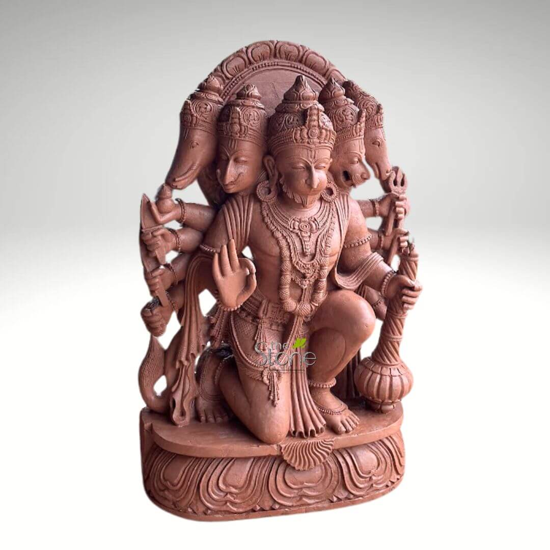 4 Feet Panchamukhi Hanuman Statue 3 detailed, reddish-brown sculpture of Panchamukhi Hanuman, a prominent Hindu deity, carved from stone or high-quality terracotta, stands prominently against a plain, light grey background. The central figure of Hanuman is depicted in a dynamic, kneeling posture, with his right knee raised and left knee resting on the intricately carved double-lotus pedestal. He wears an ornate crown, elaborate necklaces, armlets, and a dhoti. His central, human-like face has a serene yet determined expression, complete with a sculpted beard. Behind and around his primary head, four additional divine faces are visible, forming the iconic Panchamukhi (five-faced) manifestation, each wearing a crown. To his left (viewer's right) is an elephant-headed deity, possibly representing Ganesha or Hayagriva. To his right (viewer's left) is a fierce lion head, clearly identifiable as Narasimha. Above the elephant head is a bird-like head, likely Garuda, and above the lion head is another powerful animal head, which appears to be Varaha (the boar incarnation). Hanuman is portrayed with multiple arms, symbolizing his immense power and diverse abilities. His primary right hand is raised in the Abhaya Mudra, a gesture of fearlessness and blessing. His primary left hand firmly grasps a powerful gada (mace), an iconic symbol of his strength. Other arms skillfully hold various divine weapons and auspicious symbols, such as a bow and arrow, a discus (chakra), and possibly a trident (trishul) or conch shell, reflecting his role as a protector and warrior. The entire sculpture is exquisitely detailed with fine carving, from the delicate facial features and expressions of each deity to the intricate patterns on the jewelry, clothing, and the ornate, arch-like prabhamandala forming a halo behind the heads. The earthy, reddish-brown hue of the material gives the piece a traditional and authentic feel. This vibrant representation of Panchamukhi Hanuman, embodying strength, devotion, protection, wisdom, and the merging of divine energies, would be highly relevant for an article discussing Hindu iconography, the legend of Hanuman, devotional art, traditional Indian stone carving techniques, or the spiritual significance of multi-faceted deities.