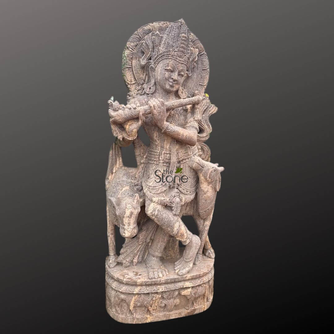 Gopala Krishna statue 5ft 4 magnificent, intricately hand-carved stone statue depicts Lord Krishna standing gracefully in a classic tribhanga (three-bend) pose, playing his Bansuri (flute). His right leg is slightly crossed over his left, and he holds the flute horizontally to his lips with both hands, evoking a sense of divine melody. Krishna's face displays a serene and joyful expression with a gentle smile, conveying peace and bliss. He wears an elaborately detailed crown (mukut) adorned with intricate patterns, possibly suggesting a peacock feather (a common attribute of Krishna), and numerous sculpted ornaments including necklaces, armlets, bracelets, and anklets. His lower garment, a dhoti, features flowing drapery and meticulous patterns, demonstrating the high level of craftsmanship. Behind his head, a beautifully carved, circular halo (prabhamandala) radiates outwards with concentric designs, symbolizing his divine aura and cosmic energy. To Krishna's left, a smaller, gentle cow or calf stands attentively, gazing upwards towards him, appearing captivated by the flute's music. The cow is also finely carved, highlighting Krishna's role as a protector of cows and a divine cowherd (Govinda). The entire sculpture is rendered in a light-colored, natural stone, possibly sandstone or a light grey marble, showcasing remarkable textural details and the artisan's skill in traditional Indian carving techniques. The statue stands on a sturdy, multi-tiered stone pedestal, which is also embellished with relief carvings, possibly floral or abstract motifs, adding to its aesthetic appeal. Presented against a plain, dark grey background, the statue is brightly illuminated, emphasizing every exquisite detail of the carving and its three-dimensional form. This devotional artwork is a prime example of Indian religious sculpture, suitable for a puja room, home altar, garden, or as a striking piece of spiritual decor or art collection, connecting viewers to Hindu mythology and the divine essence of Krishna.