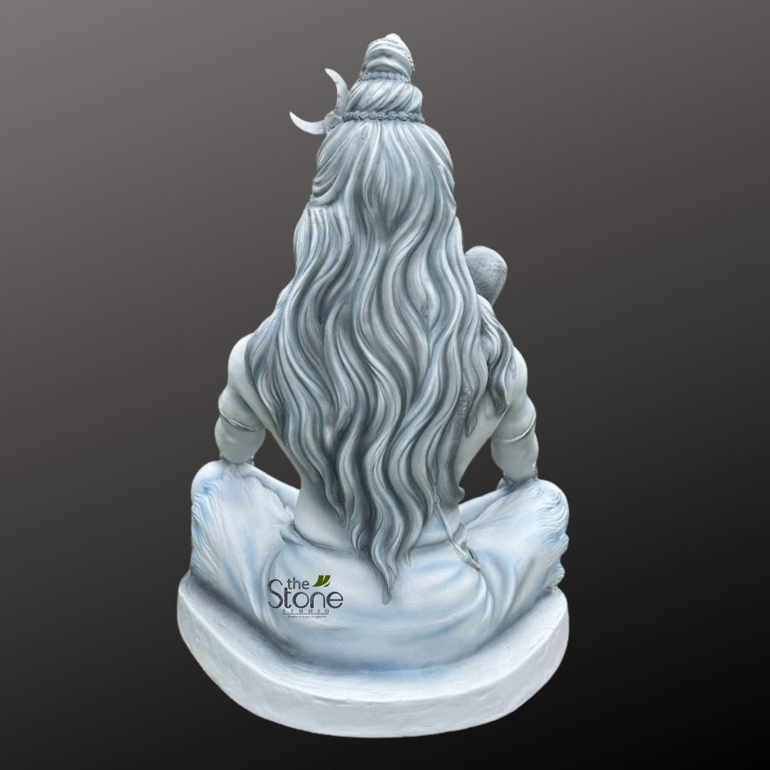 Shiv ji Murti 3ft 7 majestic stone sculpture of Lord Shiva, depicted from a rear perspective, is seated in a serene meditative posture (likely Padmasana or a similar cross-legged yoga pose). The idol, crafted from what appears to be a light grey or off-white stone-like material with subtle blue undertones, exudes a profound sense of tranquility and ancient wisdom. His long, intricately sculpted matted locks (Jata) flow gracefully down his back, cascading in deeply carved wavy strands that add dynamic texture to the figure. Atop his head, a meticulously styled topknot (Jatabhara) is adorned with a delicate crescent moon (Chandra) on the left side, a classic emblem of Lord Shiva. The powerful yet tranquil form shows his bare, sculpted back and shoulders, with simple, flowing drapery (dhoti) gracefully gathered around his lower body and legs, creating soft folds as he sits upon a simple, sturdy, circular base. The entire idol is set against a smooth, dark gradient grey background, which effectively highlights the intricate details and pale color of the sculpture, making it stand out as the central focus. Subtly visible on the lower back drapery of the statue is a watermark or logo that reads "the Stone Studio" with a small green leaf motif, indicating the artisan or manufacturer of this spiritual artwork. This detailed sculpture serves as an excellent visual representation of divine serenity, spiritual practice, and the rich iconography associated with Hindu deities, making it a compelling piece for spiritual decor, religious studies, or appreciation of traditional Indian sculpture and craftsmanship.