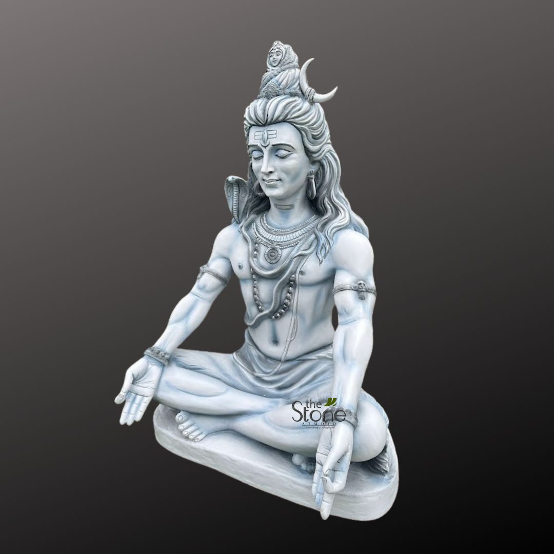 Shiv ji Murti 3ft 6 finely detailed, off-white or light grey stone sculpture depicts Lord Shiva, the prominent Hindu deity, seated majestically in a deep meditative posture, likely Padmasana (lotus pose). His eyes are gently closed, conveying an aura of profound spiritual tranquility and introspection. The intricately carved figure showcases several iconic attributes: three horizontal lines, known as the Tripundra tilaka, adorn his forehead, symbolizing his divine wisdom and the third eye. His long, flowing Jata (matted dreadlocks) are meticulously sculpted, with a crescent moon (Chandra) nestled within them and a small, serene figure representing the river Ganga gracefully emerging from the crown of his head. Around his neck, a highly detailed cobra (Naga) is coiled, its hood slightly raised, signifying his mastery over life and death. He wears multiple strands of bead necklaces, including what appears to be rudraksha beads, along with ornate armlets and wristlets. His well-defined physique highlights a blend of strength and yogic discipline. His right hand is positioned in the Chin Mudra, where the thumb and index finger gently touch, symbolizing knowledge and wisdom, while his left hand rests open in his lap, palm facing upwards. The sculpture rests on a simple, flat base and is presented against a plain, dark grey background, allowing its exquisite craftsmanship and spiritual essence to stand out. A subtle watermark for "the Stone Studio" is visible in the lower right, indicating the origin or artisan of this beautiful piece, making it relevant for articles discussing Hindu religious art, spiritual sculptures, home decor, or the significance of Lord Shiva in mythology and meditation.