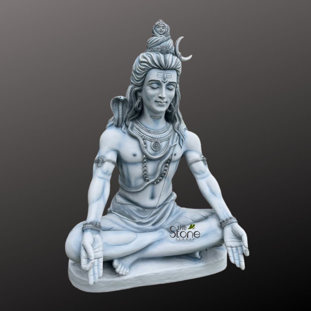 Shiv ji Murti 3ft 4 highly detailed, monochrome sculpture of Lord Shiva, the prominent Hindu deity, is showcased against a plain, dark grey background, emphasizing its intricate artistry and spiritual gravitas. The idol appears to be carved from a light grey or off-white stone or marble, giving it a classic, timeless aesthetic. Lord Shiva is depicted in a profound meditative posture, seated in the Padmasana (lotus position), with his legs crossed and feet resting on his thighs. His eyes are gently closed, conveying deep introspection and an aura of serene tranquility, with a prominent vertical mark on his forehead symbolizing his 'third eye' (Tripundra). His long, matted locks (Jatadhar) are piled high on his head, from which a small, intricately carved figure, representing Goddess Ganga, subtly emerges. Adorning the side of his hair is a distinct crescent moon, another iconic symbol associated with Shiva. Around his muscular neck, a hooded cobra (Naga) is coiled gracefully, its head subtly raised behind his left shoulder, signifying mastery over fear and poison. He wears multiple strands of necklaces: a prominent, elaborate choker-style piece close to his neck, and a longer mala (garland of beads), likely rudraksha, draping elegantly over his bare chest. Armbands (bajubandh) adorn his upper arms, and bracelets (kadas) are visible on his wrists. His hands rest gently on his knees, palms open and facing upwards, fingers forming a precise meditative mudra (Dhyana Mudra), symbolizing concentration, enlightenment, and inner peace. A simple, elegantly draped dhoti covers his lower body, with realistic folds suggesting the texture of fabric. The entire sculpture rests on a shallow, rectangular base, matching the material and monochrome tone of the deity. The overall presentation, from Shiva's calm expression to the detailed iconography, evokes themes of yoga, meditation, spiritual discipline, and divine power, making it a compelling piece for articles discussing Hindu philosophy, devotional art, or the significance of deities like Mahadev (Shiva). A subtle "the Stone Studio" watermark is visible on the lower right side of the sculpture, indicating its origin.