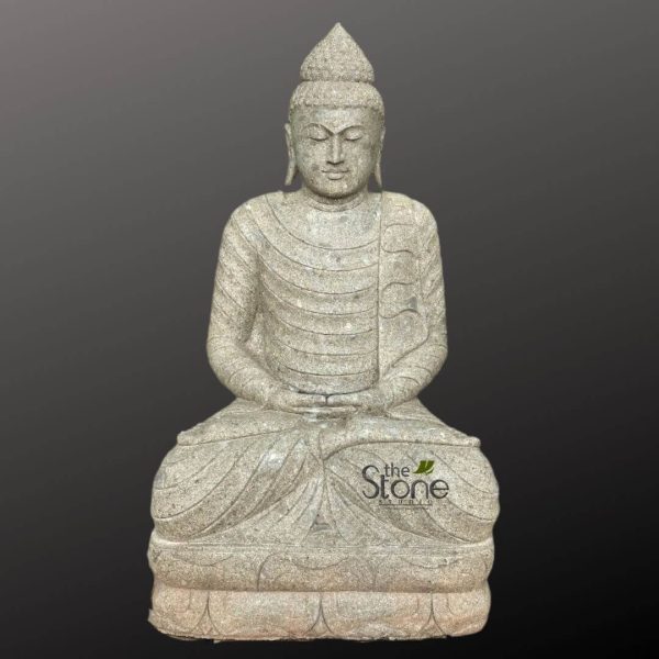 full-body, exquisitely carved stone statue of Siddhartha Gautama Buddha sits in a serene meditative posture, known as the Dhyana Mudra. The sculpture is crafted from a light, speckled grey stone, possibly granite, giving it a natural, durable, and timeless appearance with a slightly coarse yet refined texture. The Buddha is depicted with closed or gently downcast eyes, conveying deep tranquility, inner peace, and a subtle, compassionate smile on his lips. His elongated earlobes touch his shoulders, a traditional iconographic feature. A prominent Ushnisha, the cranial bump symbolizing wisdom and enlightenment, is visible on his head, topped with a distinct, pointed chignon. His hair is styled in tight, stylized curls. He is adorned in flowing monastic robes, draped gracefully over his body with horizontal folds and soft curves that suggest natural fabric. His left shoulder is covered, while the right shoulder is partially exposed, revealing the natural contours of the stone beneath. Both hands rest gently in his lap, palms facing upwards, with the right hand placed over the left, forming the classic meditation gesture. The Buddha is seated in a full lotus position (Padmasana), cross-legged, upon a meticulously sculpted double-lotus pedestal base. The individual lotus petals on the base are clearly defined, adding an elegant detail to the sculpture. The entire statue stands against a plain, dark grey or charcoal background, which allows the light grey stone and intricate details of the carving to stand out prominently without distraction. A subtle "The Stone Studio" logo is visible on the lower right side of the statue, indicating its origin. This detailed stone Buddha statue embodies mindfulness and spiritual devotion, making it a powerful visual for articles discussing Buddhist art, meditation practices, spiritual decor, garden sculptures, or the craftsmanship of natural stone.