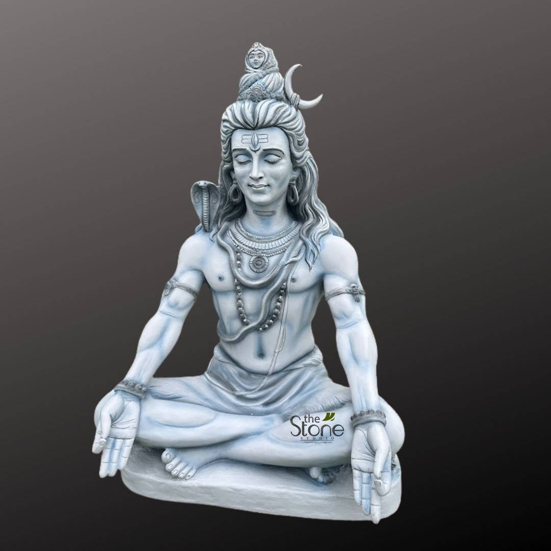 Shiv ji Murti 3ft 3 magnificent, full-body statue of the Hindu deity Lord Shiva, rendered in a serene and powerful meditative posture, is prominently displayed against a plain, dark grey gradient background. The sculpture, likely crafted from light grey or white stone such as marble or granite, exhibits remarkable detail and a smooth, polished finish, emphasizing its artisanal quality. Shiva is depicted seated in Padmasana (lotus pose), cross-legged on a simple, elevated base. His eyes are gently closed, conveying profound inner peace and deep contemplation, with a distinct third eye (Trinetra) clearly marked on his forehead, symbolizing wisdom and insight. His characteristic matted hair (jata) is piled high in a topknot, from which a delicate crescent moon (Chandra) emerges, and a miniature, sculpted figure of the goddess Ganga is visible, representing the sacred river's descent. Around his neck and shoulders, a highly detailed cobra (Vasuki) is gracefully coiled, its hood raised slightly, acting as a protector and symbol of divine power. He wears multiple strands of beaded necklaces, possibly Rudraksha beads, along with a larger, ornate pendant. Intricate armbands and wristlets adorn his strong, muscular physique. His hands rest gently on his knees in the Jnana Mudra (or Gyan Mudra), where the thumb and index finger touch, symbolizing knowledge, wisdom, and spiritual awakening. Shiva's lower body is draped in a simple, flowing dhoti or loincloth, sculpted with realistic folds. The entire statue is presented to highlight its spiritual presence and the exquisite artistry of the carving. A subtle watermark for 'The Stone Studio' is visible in the lower right portion of the image, identifying the artisan or manufacturer of this devotional artwork. This detailed representation of Mahadev embodies tranquility, spiritual power, and the profound iconography associated with Hindu worship and meditation practices, making it a focal point for any discussion on Hindu deities, spiritual decor, or traditional Indian stone craftsmanship.