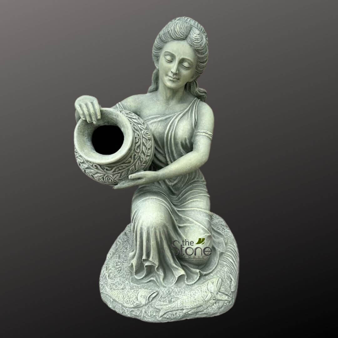 Sitting Lady Water Fountain 3ft 5 full-body studio shot of a serene, classical-style female garden sculpture, rendered in a muted, antique grey-green finish. The graceful figure is depicted kneeling or elegantly seated on an ornate, organically shaped base, with her head gently bowed and eyes closed in contemplation or peaceful repose. Her soft, classical features are framed by elegantly styled hair pulled back, adorned with subtle waves and tendrils. She is draped in flowing, single-shouldered classical attire, with intricate folds and pleats that cascade down, suggesting lightweight fabric and enhancing her delicate posture. In her hands, she holds a generously sized, rounded urn or pot with a wide, open mouth, tilting it slightly as if in the act of pouring water or displaying its contents. The pot is highly decorative, featuring deeply carved or embossed intricate floral and leafy vine patterns that encircle its entire surface, adding a rich artisanal touch. The figure rests upon an elaborately sculpted base, resembling an irregular rock formation or stylized aquatic flora, intricately textured with patterns that appear to be overlapping fish scales or subtle water ripples. The entire sculpture, likely crafted from durable cast stone, concrete, or weather-resistant resin, exhibits a beautiful, earthy grey-green hue with subtle darker antiquing, mimicking the appearance of aged stone or a verdigris patina. This finish ensures it is a long-lasting and aesthetically pleasing decorative element for outdoor spaces. The logo "the Stone Studio" is subtly visible on the base. This elegant piece is ideal for enhancing garden aesthetics, creating a tranquil focal point in a patio or courtyard, or potentially serving as a unique garden fountain element, bird bath, or planter in any landscape design.