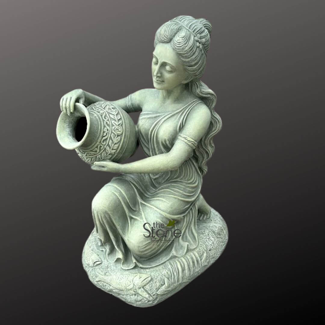 Sitting Lady Water Fountain 3ft 1 highly detailed, full-body stone statue depicts a serene female figure kneeling gracefully, angled slightly towards the viewer's left. She embodies a classical or Greco-Roman aesthetic, dressed in elegant, flowing drapery that gathers in realistic folds around her body, leaving one shoulder partially bare. Her hair is intricately styled, pulled back into an upswept bun or braid on top, with soft waves cascading over her shoulder. Her face shows a gentle, contemplative expression with downcast eyes, looking towards the ornate vessel she holds. The woman holds a decorative urn or pitcher, tilting it forward as if pouring water or offering its contents. The urn features intricate, raised relief carvings depicting a continuous pattern of leaves, vines, or perhaps a laurel wreath around its bulbous body, contrasted by a smooth neck and flared rim. Both the figure and the urn are crafted from a light grey stone with subtle greenish undertones, suggesting a weathered, aged appearance, possibly limestone, concrete, or a similar natural material. This texture is consistent with the "the Stone" watermark visible on the base. The statue rests upon an irregular, textured rock-like plinth, also made of stone, which features subtle, carved details resembling foliage or natural contours, grounding the figure. The entire sculpture is isolated against a plain, dark charcoal grey background, enhancing its sculptural presence and making the intricate details stand out. This exquisite piece, an example of fine stone craftsmanship, would serve as an elegant garden ornament, a striking outdoor sculpture, or a sophisticated indoor decorative accent. Its timeless design and depiction of a water-bearing figure suggest its connection to themes of nature, classical mythology, tranquility, and potentially as a feature for a fountain or pond, embodying the grace and artistry often sought in premium garden statues and landscape design elements.