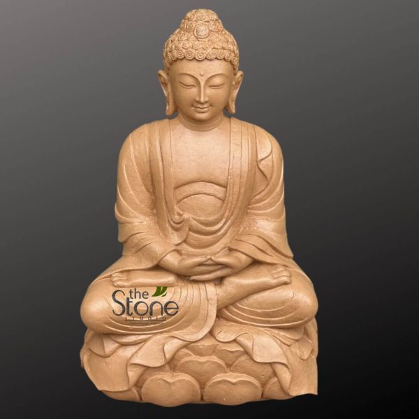 full-length, front-facing photograph of a serene Buddha statue, meticulously carved from what appears to be natural sandstone or a similar light brown, earthy-toned material. The statue depicts Siddhartha Gautama seated in a classic meditative posture, likely Padmasana (lotus position), with legs crossed and feet resting on the opposite thighs. His hands are gently placed in his lap, palms facing upwards in the Dhyana Mudra (meditation gesture), with the right hand resting atop the left, signifying deep concentration and the attainment of enlightenment. His face exudes profound tranquility and peace: eyes are softly closed or downcast, a faint, peaceful smile plays on his lips, and a small, prominent urna (dot of spiritual wisdom) is visible between his eyebrows. The ushnisha, the cranial protuberance symbolizing wisdom and enlightenment, is finely sculpted with numerous rows of tightly curled hair (often depicted as snail shell curls), and his earlobes are elongated, a traditional symbol recalling his princely past and subsequent detachment from worldly possessions. The flowing monastic robes are draped elegantly over his body, with naturalistic folds and creases carved into the stone, suggesting soft fabric while maintaining the solid form of the sculpture. The contours of his lean, graceful physique are subtly visible beneath the drapery. He rests upon a beautifully carved lotus flower base, featuring multiple layers of sculpted petals that symbolize purity, spiritual awakening, and perfection. The entire statue is presented against a plain, dark gray or charcoal background, which allows its warm, monochromatic hue and intricate details to stand out prominently without distraction. A small, subtle logo for "the Stone Studio" is visible on the lower left side of the image, indicating the craftsmanship or origin. This exquisite piece embodies calm and mindfulness, making it an ideal representation for articles on spiritual decor, meditation practices, artisan stone carvings, Asian art, or objects promoting peace and tranquility in living spaces.