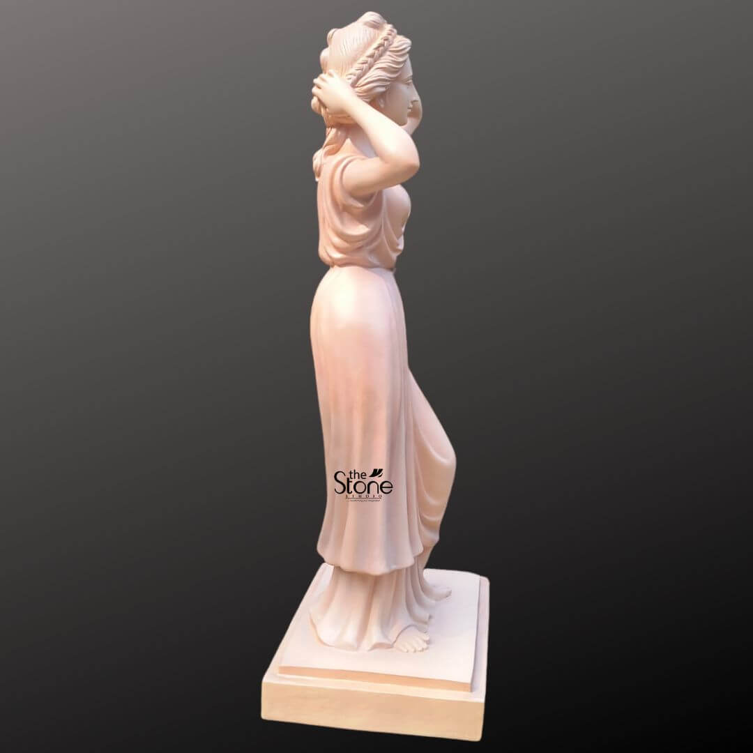 Angel Lady Statue for Resorts 5.5 Feet 5 An elegant side-profile view of a 5.5-foot Angel Lady Statue, masterfully crafted from high-quality, durable fibre. This life-sized sculpture is specifically designed to enhance the aesthetic of luxury hotels, resorts, and upscale commercial spaces. The classical female figure is depicted in a graceful posture with her hands raised to her intricately braided hair, conveying a sense of timeless beauty. She wears a floor-length, flowing gown with delicately carved drapery that adds a sophisticated sense of movement to the piece. The statue features a smooth, pale terracotta-toned finish and stands securely on a sturdy, square tiered pedestal. Its impressive 5.5 ft height makes it an ideal focal point for grand hotel lobbies, elegant corridors, or outdoor resort gardens, perfectly blending classical artistic style with modern, lightweight durability.