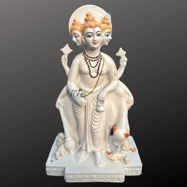 An exquisitely detailed Lord Dattatreya fibre statue, depicting the unified form of the Hindu Trinity—Brahma, Vishnu, and Shiva—in a majestic standing pose. The sculpture features three serene heads, each adorned with orange-tinted matted hair (jata) and a traditional red tilak, symbolizing divine wisdom and spiritual illumination. This six-armed deity is masterfully crafted from high-quality, lightweight fibre material, making it a durable and weather-resistant alternative to traditional stone or marble. The idol is shown holding sacred spiritual symbols, including the Sudarshana Chakra (discus) and Shankha (conch shell), while wearing multiple layers of realistic bead necklaces. Adding to the rich Vedic iconography, the Dattatreya statue includes the sacred Kamadhenu cow standing protectively behind him and four small dogs at his feet, representing the four Vedas. The entire figure stands on a multi-tiered white pedestal embellished with traditional relief patterns. With its smooth white finish and subtle color accents, this fibre Dattatreya idol serves as a profound spiritual centerpiece for a home mandir, meditation sanctuary, or an elegant garden landscape, inviting peace, knowledge, and prosperity into the surroundings.