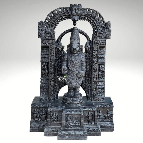 An exquisitely hand-carved 36-inch blackstone Lord Venkateswara Tirupati Balaji Murti, designed with a rustic finish to bring the spiritual essence of the Tirumala temple into a home sanctuary. This detailed sculpture features the deity in a majestic standing posture atop a circular lotus pedestal. Lord Venkateswara is adorned with traditional temple ornaments, including a towering tiered crown (Kiritamukuta), elaborate necklaces, and the signature wide sacred tilak (Namam) on his forehead. The central figure is framed by a grand and highly intricate Prabhavali (ornate archway), which features a protective Kirtimukha (lion-faced) crest at the very top. The side pillars of the arch are deeply engraved with scrollwork and smaller figures of celestial attendants. The deity’s upper hands hold the sacred Sudarshana Chakra (discus) and the Panchajanya Shankha (conch), while his lower hands are held in the traditional mudras of blessing and protection. The entire blackstone statue rests on a wide, multi-tiered rectangular base. This pedestal is a work of art in itself, featuring narrative panels that depict the Dashavatara (ten incarnations of Lord Vishnu) in high relief. The deep, charcoal-black hue of the stone highlights the fine details of the carving, giving the Tirupati Balaji Murti a timeless and powerful presence. This 3-foot-tall spiritual icon is an ideal centerpiece for a home temple, meditation room, or an elegant garden alcove, inviting divine energy and peace.