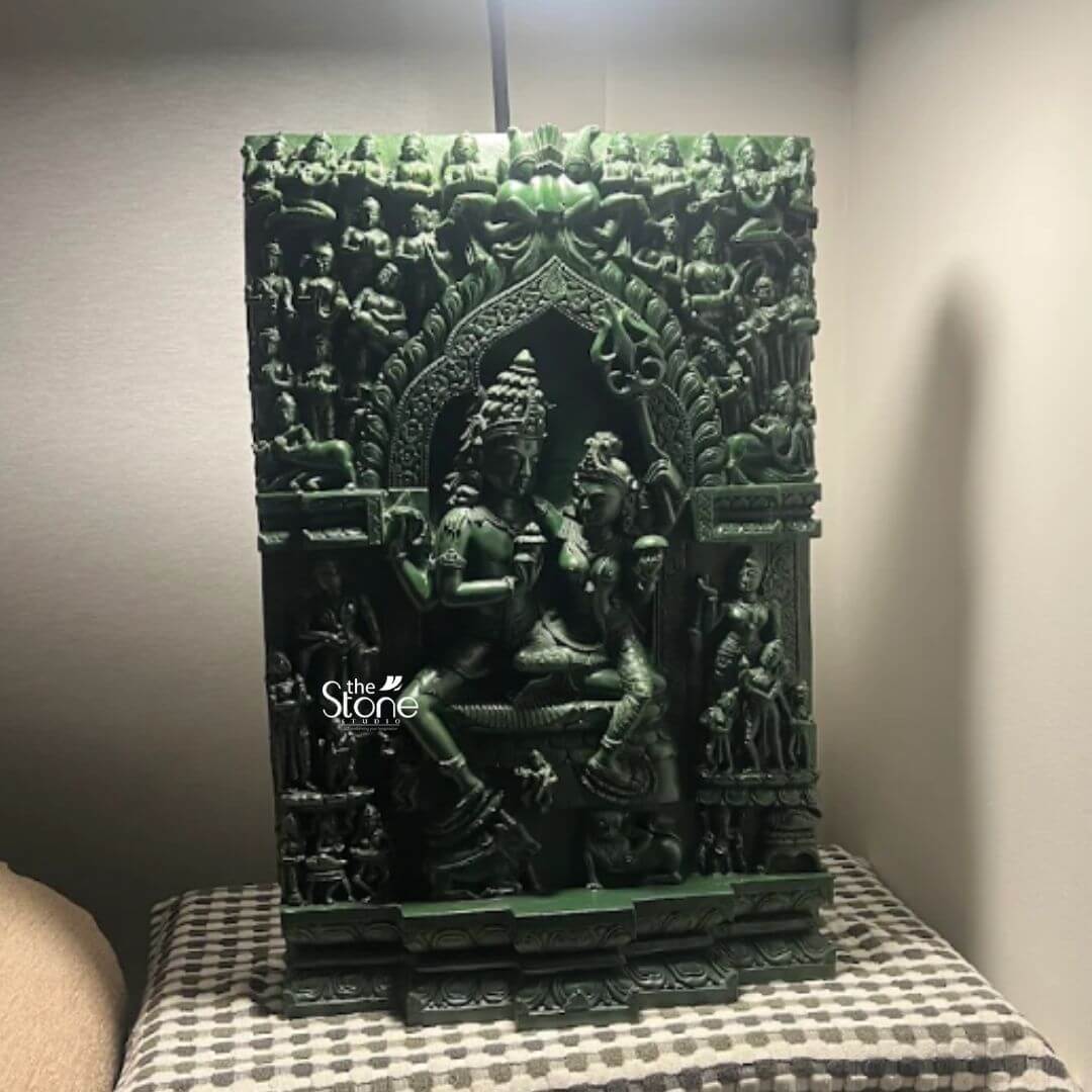 Shiva Mural 2ft 2 A captivating green stone Shiva Parvati statue intricately carved as a wall panel is prominently displayed indoors serving as a powerful spiritual and artistic statement. The statue depicts Lord Shiva and Goddess Parvati seated together in a tender embrace surrounded by a multitude of smaller deities and mythological figures all meticulously carved from a deep rich green stone. This exquisite piece embodies divine harmony and creation making it a significant cultural and spiritual artifact in a home in Melbourne Australia. The central figures of Shiva and Parvati are adorned with elaborate crowns jewelry and traditional attire their forms conveying serenity and devotion. Shiva holds his trident while Parvati sits gracefully beside him their expressions serene and loving. The architectural frame around them is incredibly detailed resembling a temple archway intricately decorated with celestial beings musicians and other mythological creature all contributing to the grandeur and narrative depth of the sculpture. The high relief carving creates a striking play of light and shadow bringing the stone to life. This green stone Shiva Parvati statue is a profound representation of divine love power and the cosmic union perfectly suited for a prominent display in a home in Melbourne Australia. The choice of green stone often associated with growth renewal and healing enhances its spiritual significance. As a hand-carved piece it speaks to centuries of artistic tradition and devotional practice enriching any space with its deep cultural resonance and serving as a focal point for spiritual contemplation and appreciation of sacred art.