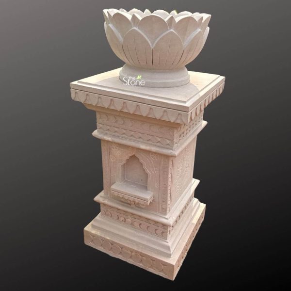An exquisitely hand-carved stone Tulsi Vrindavan made from natural off white sandstone, serving as a sacred and decorative centerpiece for a traditional Indian garden or home courtyard. This architectural masterpiece features a multi-tiered pedestal design, topped with a planter bowl meticulously sculpted in the shape of a blooming lotus flower, symbolizing purity and spiritual devotion.The central column of the structure is adorned with intricate geometric borders and delicate floral relief carvings. A key functional and aesthetic feature is the recessed arched niche on the front, traditionally designed to hold an oil lamp or diya during daily prayer rituals. The sturdy, wide base is finished with repeating circular patterns, providing stability for outdoor placement while enhancing its timeless, rustic appeal. This sandstone Tulsi Vrindavan combines high-quality stone craftsmanship with spiritual significance, creating a durable and weather-resistant sanctuary for the holy basil plant. Its earthy tones and detailed masonry make it a perfect focal point for garden decor, inviting peace, positive energy, and a sense of sacred tradition into the home environment.