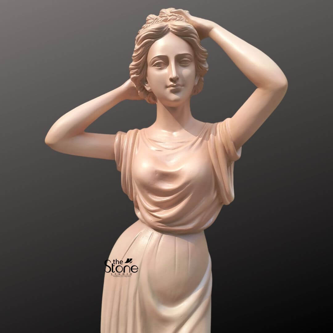 Angel Lady Statue for Resorts 5.5 Feet 3 A close-up view of an elegant 5.5-foot unique lady sculpture, meticulously crafted from durable, high-quality fibre. This life-sized classical figure is depicted in a poised and graceful stance, with her arms delicately raised behind her head as she adjusts her wavy, styled hair. Her facial expression is serene and gentle, embodying a sense of timeless beauty that makes it an ideal centerpiece for luxury resorts or grand hotel lobbies. The sculpture is clad in a classical sleeveless gown, featuring masterfully sculpted flowing drapery with realistic folds that highlight the fine artistic craftsmanship. The smooth, soft peach-toned finish adds a sophisticated touch to the piece. Standing at 5.5 ft tall, this fibre statue is designed to be both lightweight and resilient, making it a perfect spiritual and aesthetic addition to upscale garden settings, poolside areas, or grand entrances.