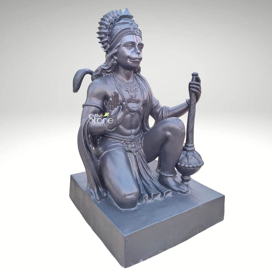 3 Feet Hanuman Ji Statue 5 A majestic 3-foot tall Lord Hanuman statue masterfully hand-crafted from high-quality fibre material, serving as a powerful spiritual focal point for home or garden decor. The sculpture depicts the deity in a powerful kneeling posture, representing his immense strength and unwavering devotion. Lord Hanuman’s right hand is raised in the Abhaya Mudra, the universal gesture of protection and blessing, while his left hand firmly holds a large Gada (mace) resting on a solid rectangular pedestal. The statue is finished in a sophisticated matte black charcoal tone, accentuating the fine artisan details of his tiered sunburst crown, layered necklaces, and the realistic fluid folds of his traditional dhoti. Designed to be durable and weather-resistant, this large-scale 36-inch fibre Hanuman idol is a perfect addition to a grand home mandir, garden sanctuary, or professional foyer, inviting an atmosphere of courage and divine peace into any modern or traditional living space.