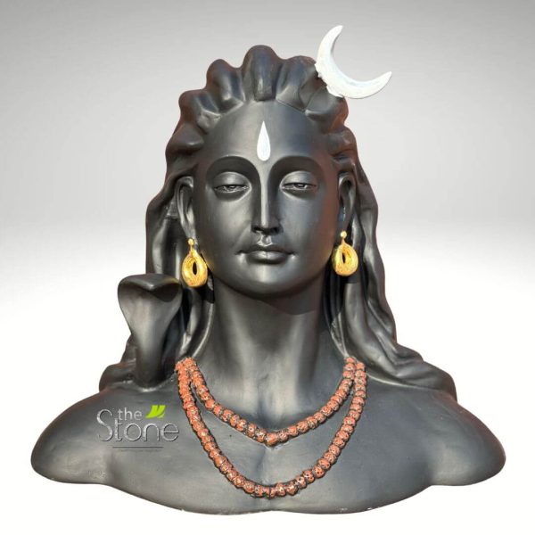 An exquisitely detailed 18-inch Adiyogi Shiva fibre statue, masterfully crafted to represent the first yogi and the source of yoga. This spiritual bust sculpture is finished in a smooth, matte charcoal black, offering a sophisticated and serene aesthetic perfect for a meditation room, yoga studio, or home altar. The statue captures Lord Shiva in a deep meditative state with a calm facial expression and closed eyes. Iconic spiritual symbols are rendered with precision: a bright white crescent moon is nestled in his flowing matted hair, and a white teardrop-shaped tilak is prominently marked on his forehead. He is adorned with traditional golden hoop earrings and two long, textured rows of reddish-brown Rudraksha bead necklaces. Behind his right shoulder, the hood of a sacred cobra serpent is visible, adding to the authentic Vedic iconography. Made from high-quality, lightweight, and durable fibre material, this 18-inch Adiyogi idol combines traditional Indian artistry with modern durability, creating a powerful centerpiece that invites peace, mindfulness, and divine energy into any living space.