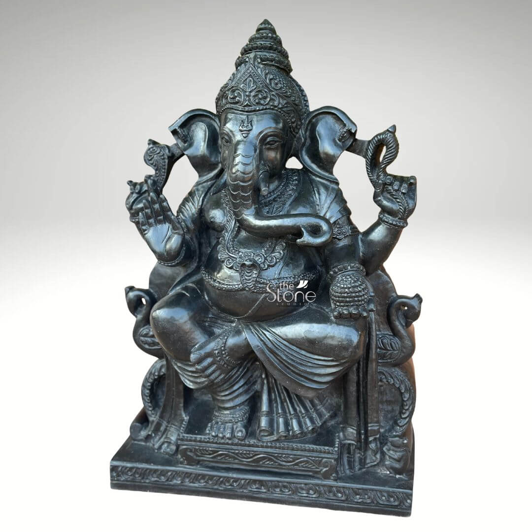 Black Stone Ganesha Idol for Entrance 2ft 6 An exquisitely hand-carved 2-foot tall black stone Ganesha idol, masterfully sculpted from premium natural black stone to serve as a majestic centerpiece for a professional office foyer or a home mandir. This 2ft Ganesha statue captures the deity in a stable and auspicious seated posture atop an intricately detailed, multi-tiered pedestal embellished with traditional relief carvings. Lord Ganesha is portrayed with four arms carrying sacred symbols, with his lower right hand raised in the Abhaya Mudra, the universal gesture of protection and blessing. The craftsmanship highlights incredible detail, from the towering tiered crown (mukut) and large expressive ears to the layered necklaces and realistic fabric folds of his traditional attire. The refined matte charcoal finish of the blackstone Ganesha sculpture radiates an aura of wisdom, stability, and professional elegance, making it a perfect addition to invite peace and the removal of obstacles into any contemporary or traditional workspace.