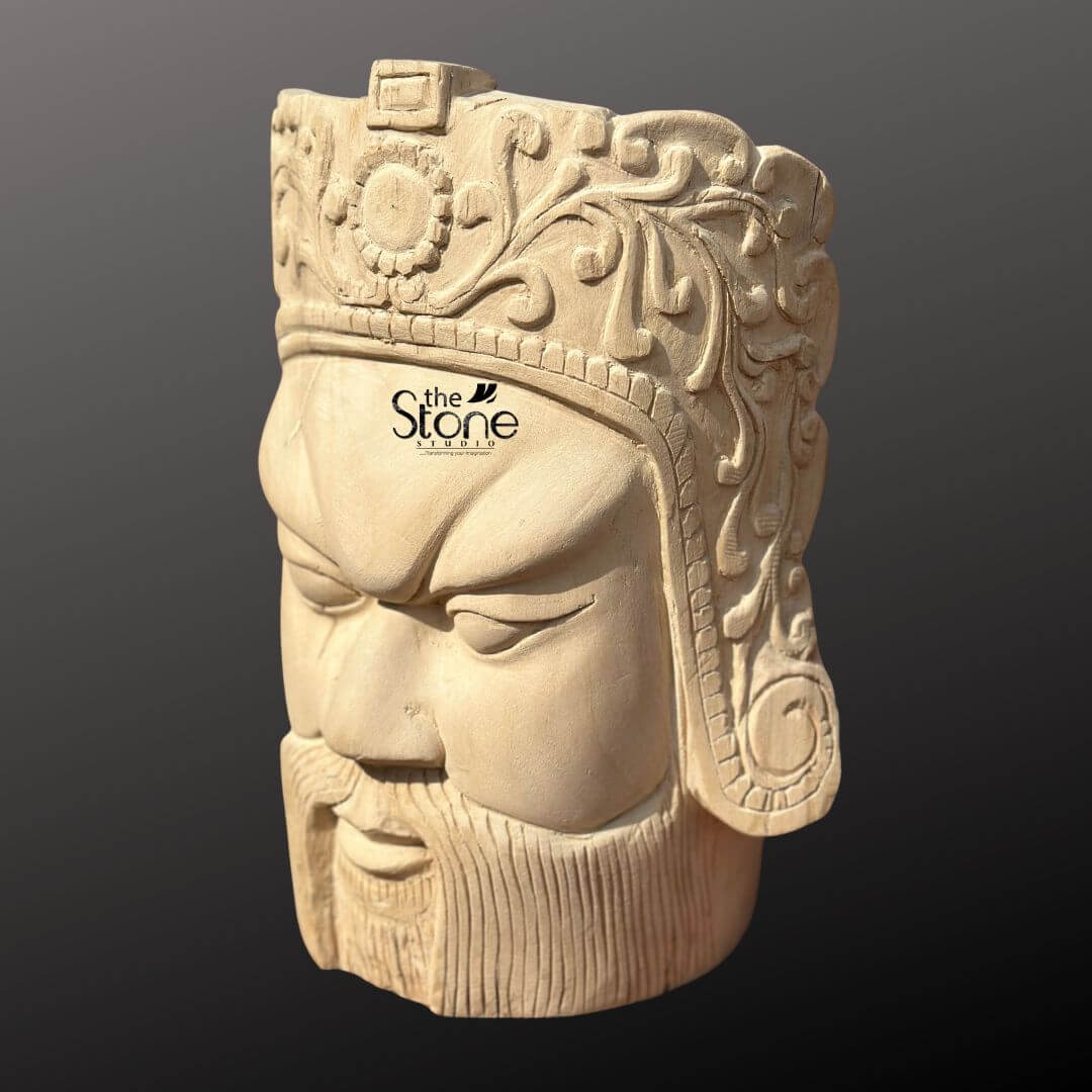 Royal Head Sculpture 12" 5 This image showcases a finely detailed 12-inch Hand Carved Heritage Style Sculpture of a male head expertly crafted from light-colored wood. The sculpture is presented against a dark, neutral background, emphasizing its intricate details and the natural texture of the wood. The face features strong, angular characteristics consistent with a heritage style including deeply furrowed brows intense, narrow eyes that gaze downward, a straight nose, and a firmly closed mouth adorned with a full, sculpted beard and mustache. The expression conveys a sense of stern authority and ancient wisdom, evocative of historical or mythological figures. Crowning the head is an elaborate headdress or helmet, richly decorated with intricate floral and scrollwork patterns, a central circular emblem (possibly a sun or stylized flower), and patterned bands. The precision of the hand-carved details is remarkable, with every element meticulously shaped from the single piece of wood. The natural grain of the wood is visible throughout the sculpture, particularly on the face and beard, adding to its authentic and rustic yet refined appearance. This wooden head sculpture truly embodies a sense of heritage and artisanal skill, making it a compelling piece for collectors or as a distinctive decorative item.