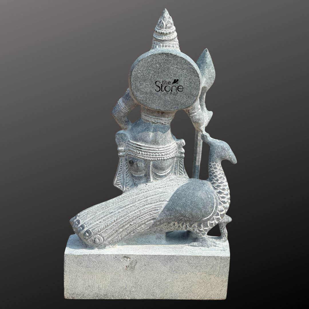 Lord Skanda Murugan Stone Statue 15" 8 A rear perspective of an exquisitely hand-carved 15-inch Lord Kartikeya statue, masterfully sculpted from natural blackstone with a rustic, weathered finish. This back view highlights the exceptional 360-degree craftsmanship of the idol, showcasing the intricate details of the deity’s towering tiered crown (mukut) and the layered carvings of his traditional attire and decorative waistband. Lord Kartikeya is accompanied by his divine vehicle, the peacock, which is gracefully positioned at the base of the sculpture. The peacock features meticulous relief work on its neck and tail feathers, reflecting the precision of traditional Indian stone masonry. The entire blackstone Murugan idol rests on a solid, unpolished rectangular pedestal, emphasizing the organic and earthy beauty of the natural stone. This compact and durable spiritual sculpture is an ideal addition to a home mandir, garden sanctuary, or personal altar, providing a sense of ancient temple heritage and divine protection to any living space.