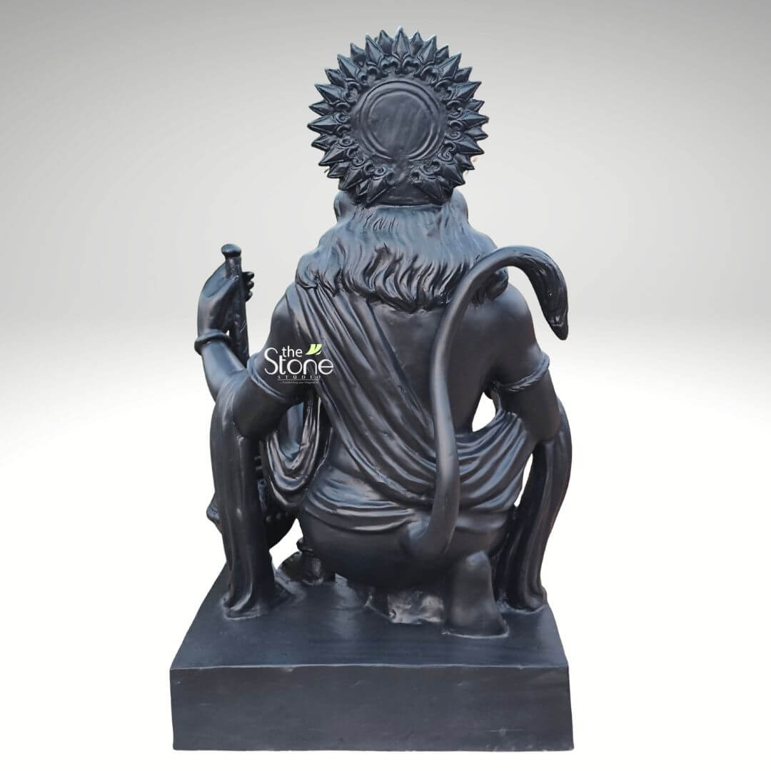 3 Feet Hanuman Ji Statue 6 A rear view of a majestic 3-foot tall Lord Hanuman Ji fibre statue, masterfully hand-crafted to serve as a powerful spiritual centerpiece for home or garden decor. The sculpture depicts the deity in a traditional kneeling posture on a solid rectangular base, showcasing the exceptional 360-degree craftsmanship of the piece. The back view highlights the intricate patterns on his sunburst-style tiered crown (mukut) and the realistic, fluid folds of his traditional dhoti. Lord Hanuman’s iconic long tail curves gracefully from his back, looping up over his shoulder. This large-scale 36-inch fibre Hanuman idol features a refined matte charcoal black finish that mimics natural stone while remaining lightweight and durable. This perspective emphasizes the sculpture's balanced proportions and high-quality finish, illustrating its suitability for creating a peaceful meditation sanctuary or an auspicious home entrance, designed to invite strength and divine protection into any environment.