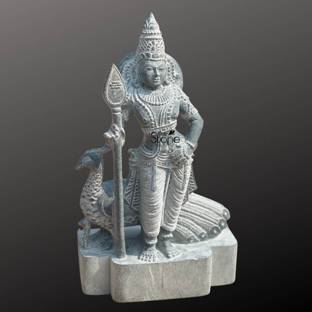 Lord Skanda Murugan Stone Statue 15" 4 An exquisitely hand-carved 15-inch Lord Kartikeya stone statue, masterfully crafted from premium natural blackstone to serve as a powerful spiritual centerpiece. The deity, also known as Murugan or Skanda, is depicted in a majestic standing posture, holding his iconic Vel (sacred spear) in his right hand, which symbolizes divine wisdom and the destruction of ignorance. Lord Kartikeya is adorned with an intricately detailed tiered crown (mukut), layered necklaces, armlets, and traditional ornaments that showcase the depth of Indian stone craftsmanship. Standing faithfully behind the Lord is his divine vehicle, the peacock (vahana), with its head visible to the left and its tail feathers delicately rendered in relief to the right. The blackstone Murugan idol features a rustic, weathered finish that highlights the fine textures of the stone masonry and the realistic folds of his traditional attire. Resting on a sturdy, multi-lobed stone pedestal, this 15-inch spiritual sculpture is an ideal size for a home mandir, personal altar, or meditation corner. It captures the serene yet strong essence of the deity, inviting an atmosphere of protection, victory, and peace into any living space.