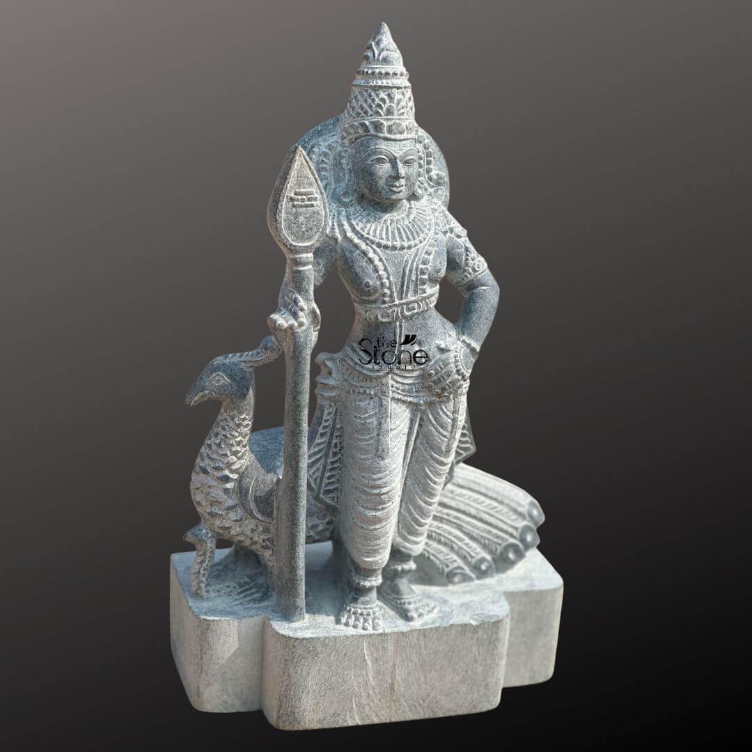 Lord Skanda Murugan Stone Statue 15" 6 An exquisitely hand-carved 15-inch Lord Murugan stone statue, masterfully sculpted from premium natural blackstone to serve as a powerful spiritual centerpiece. The deity, also known as Kartikeya or Skanda, is depicted in a majestic standing posture, holding his iconic Vel (sacred spear) in his right hand, which symbolizes divine wisdom and the destruction of ignorance. Lord Murugan is adorned with an intricately detailed tiered crown (mukut), layered necklaces, armlets, and traditional ornaments that showcase the depth of Indian stone craftsmanship. Standing faithfully behind the Lord is his divine vehicle, the peacock (vahana), with its tail feathers delicately rendered in relief. The blackstone Murugan idol features a rustic, weathered grey finish that highlights the fine textures of the stone masonry and the realistic folds of his traditional attire. Resting on a sturdy, multi-lobed stone pedestal, this 15-inch spiritual sculpture is an ideal size for a home mandir, personal altar, or meditation corner. It captures the serene yet strong essence of the deity, inviting an atmosphere of protection, victory, and peace into any living space.