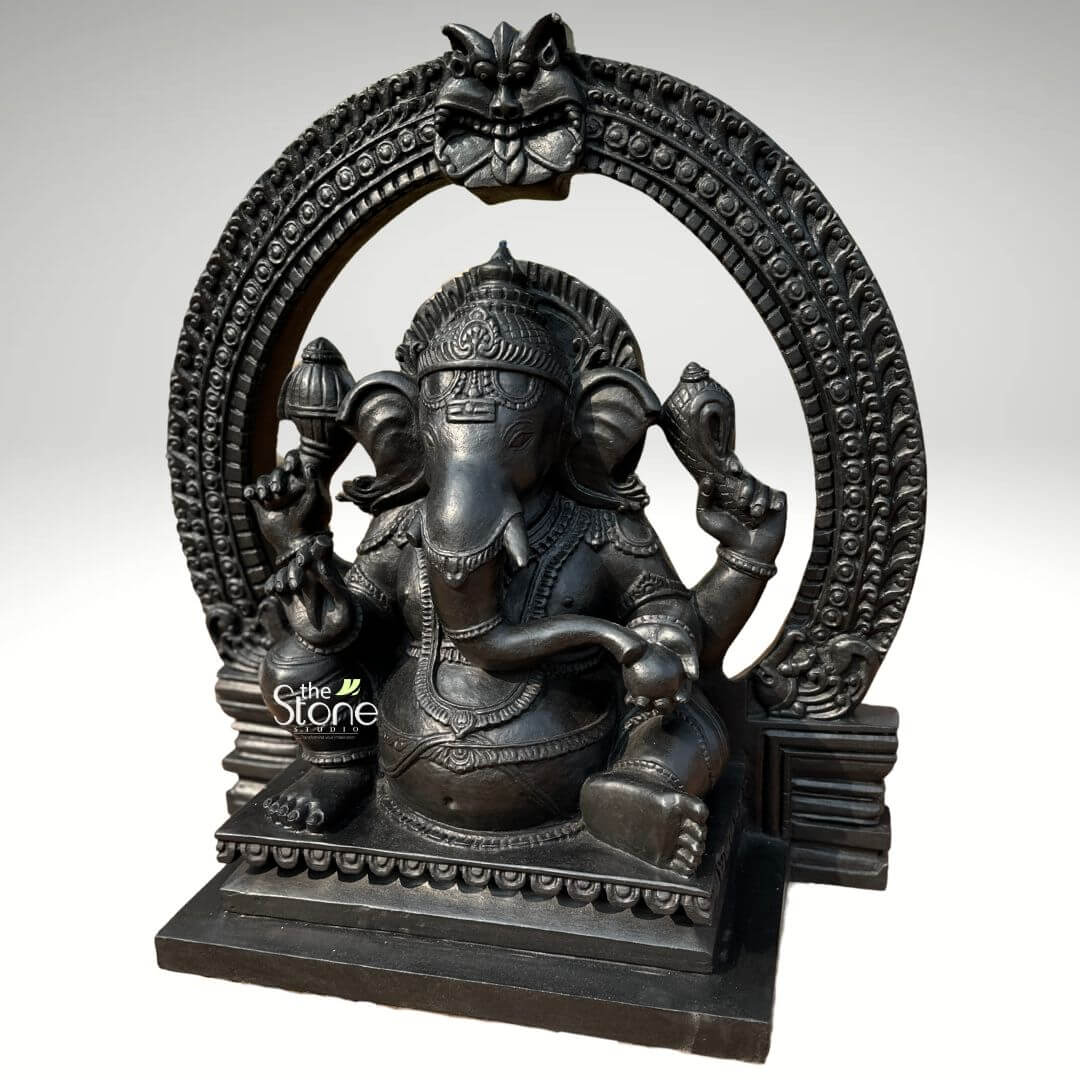 Vighnaharta Ganesh Idol 2ft 8 An exquisitely crafted 24-inch sitting Lord Ganesha statue with a majestic Torana (ornate arch), designed as a powerful spiritual centerpiece. This 2-foot fibre statue features a refined black stone finish, capturing the heavy and timeless aesthetic of natural blackstone in a lightweight, durable form. The deity is depicted in a stable seated pose on a multi-tiered rectangular pedestal decorated with lotus-petal relief. Lord Ganesha has four arms, holding traditional spiritual symbols including a Gada (mace) and a Shankha (conch shell), while his large ears and curved trunk symbolize divine wisdom and the removal of obstacles. He is beautifully adorned with a towering tiered crown (mukut), layered necklaces, and traditional ornaments with realistic fabric folds on his attire. Framing the entire figure is a grand, circular Torana or Prabhavali, meticulously carved with rhythmic patterns and topped with a protective Kirtimukha face, evoking the architectural beauty of ancient temples. This black stone-finish Ganesha idol is an ideal addition to a home mandir, office entrance, or meditation space, inviting peace, stability, and auspicious energy into any living or professional environment.