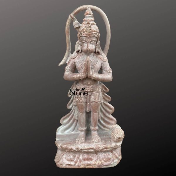 An exquisitely hand-carved 12-inch small Hanuman stone statue made of natural pinkstone, depicted in a humble standing posture with hands joined in the Anjali Mudra, a traditional gesture of prayer and devotion. The sculpture showcases Lord Hanuman’s iconic long tail curving gracefully behind his head and a detailed tiered crown (mukut) that reflects masterful Indian craftsmanship. Beside his feet rests his signature weapon, the Gada (mace), atop an intricately carved lotus pedestal. The natural pinkstone material features an earthy, rustic texture with beautiful organic grain patterns in shades of tan and dusty rose, giving the idol a timeless antique temple look. This compact 12-inch pinkstone Hanuman statue serves as a powerful spiritual centerpiece for a home temple, office desk, or small meditation corner, inviting an aura of strength, loyalty, and protection into any space.