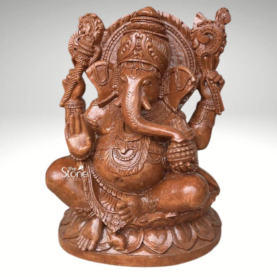 Pillaiyar Ganesha Statue 2.5ft 4 A majestic 2.5-foot tall Sri Vinayaka statue masterfully hand-carved from premium natural brown sandstone serves as a profound spiritual centerpiece for a home or garden. This large-scale black stone Ganesha idol is depicted in a stable and auspicious seated posture atop an intricate, multi-tiered lotus pedestal embellished with detailed relief carvings. Lord Ganesha is portrayed with four arms carrying sacred spiritual symbols: his upper hands hold a traditional axe and goad to guide and remove obstacles while his lower right hand is raised in the Abhaya Mudra the universal gesture of protection and blessing. His trunk curves gracefully toward his hand, representing the focus on spiritual attainment. The craftsmanship showcases incredible detail from the towering, tiered mukut and large expressive fan-like ears to the layered necklaces, armlets, and realistic fabric folds of his traditional attire. Framing the deity's head is a grand, circular Prabhavali embellished with rhythmic petal-like relief patterns that symbolize a divine aura. The refined matte finish and grainy, earthy reddish-brown texture of the sandstone give this 30-inch Vinayaka idol a timeless, antique temple aesthetic, making it a perfect addition to invite peace, prosperity, and the removal of obstacles into any contemporary or traditional living environment.